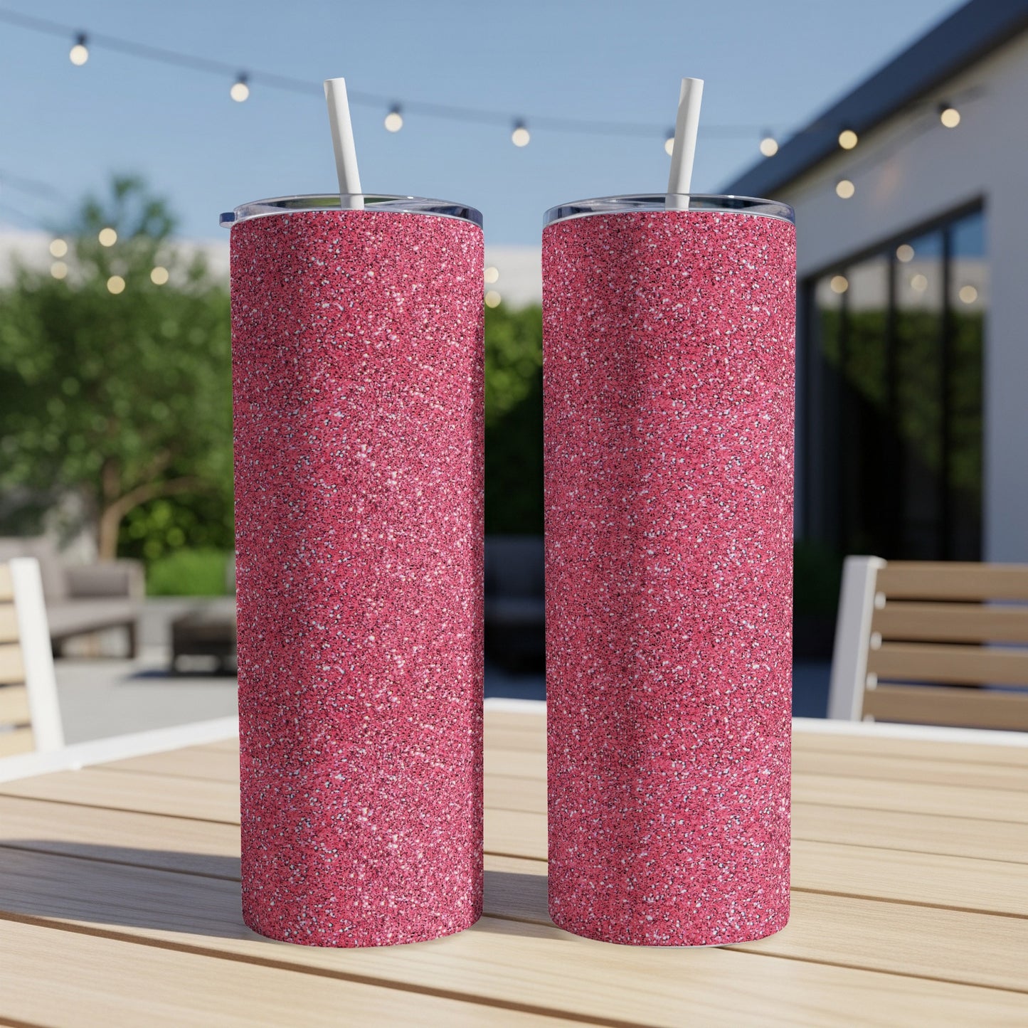 Two pink glitter tumblers with white straws stand on a wooden table.