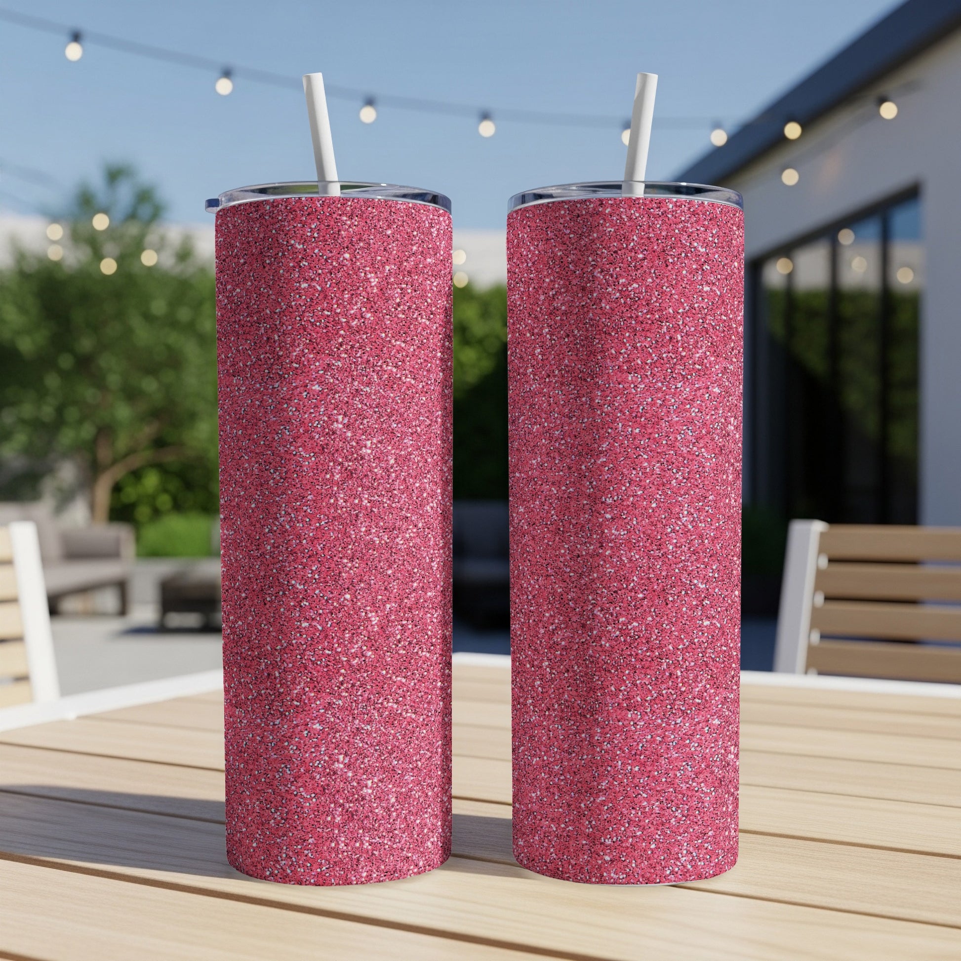 Two pink glitter tumblers with white straws stand on a wooden table.