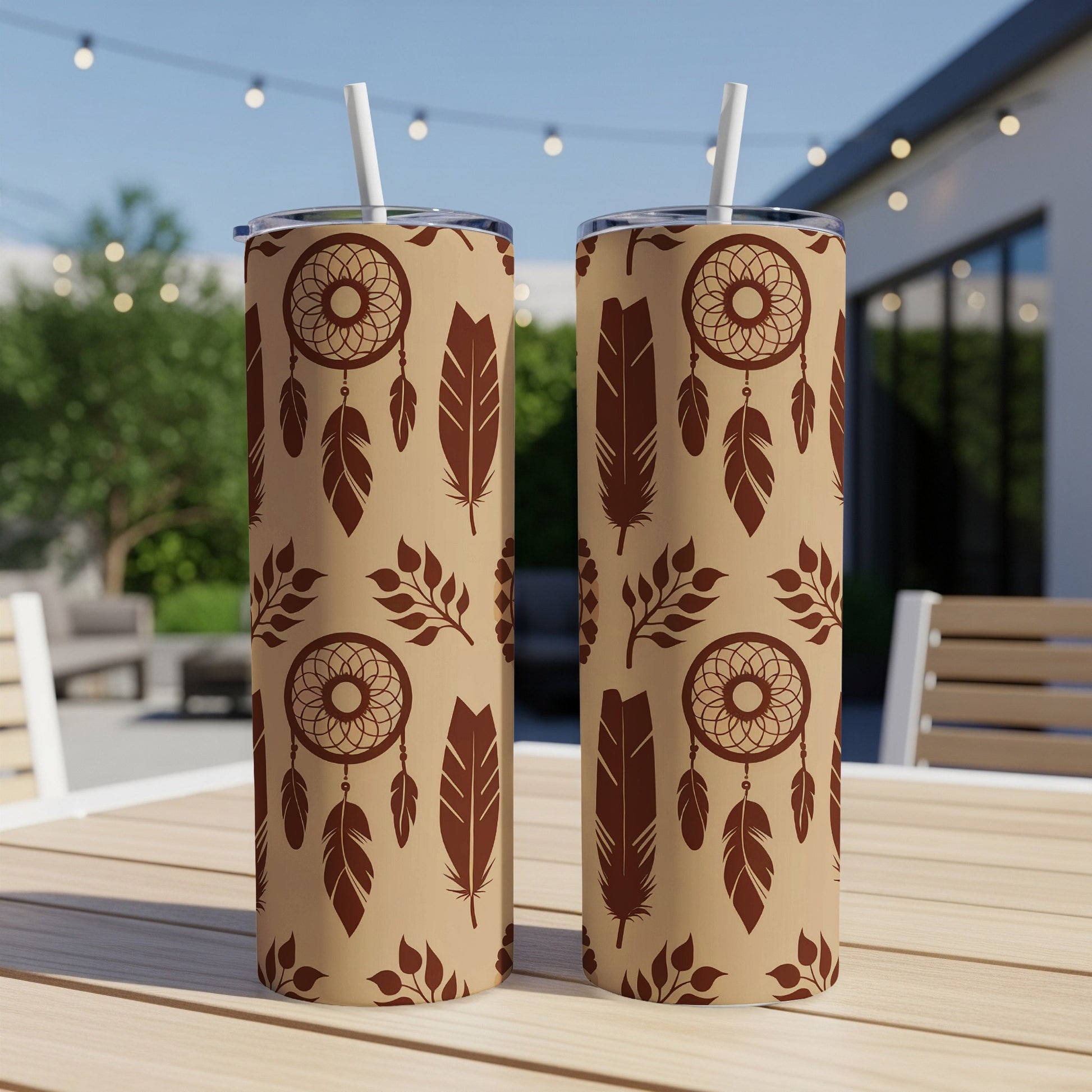 Two tall, patterned tumblers with dreamcatcher and feather designs on a table.