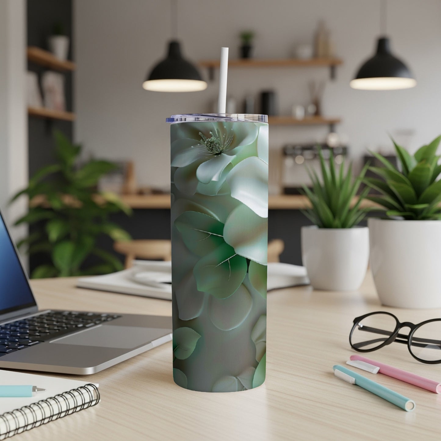 White floral pattern tumbler with straw on a desk with laptop and pens.