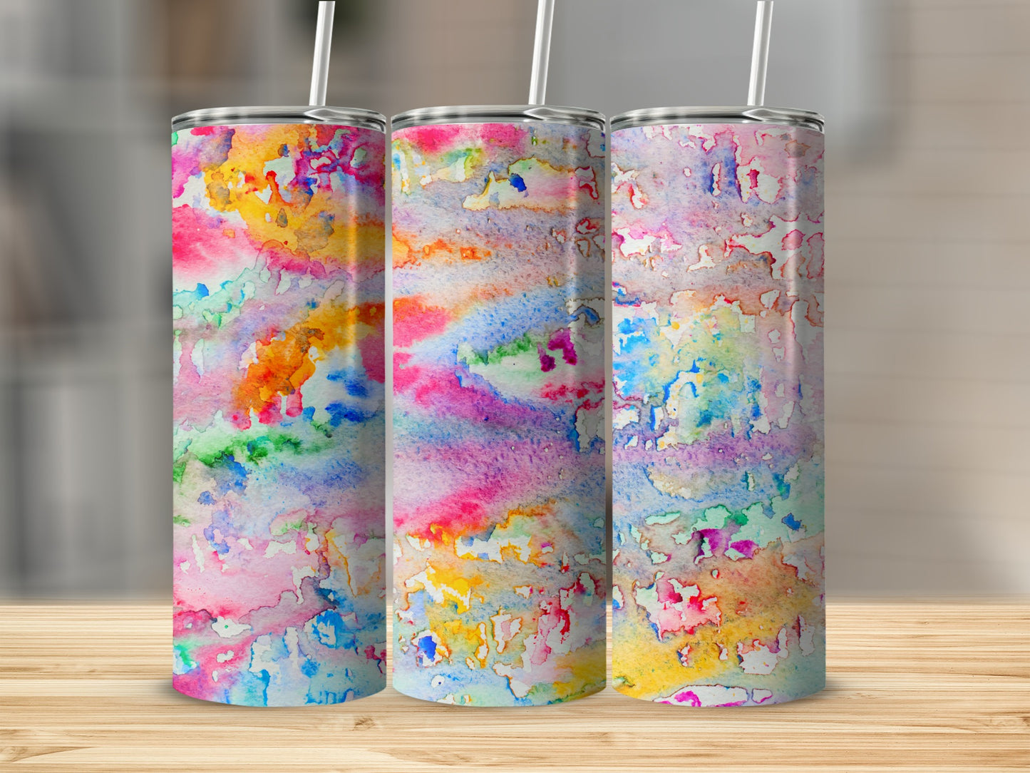 Three tumblers with colorful watercolor patterns on a wooden surface.