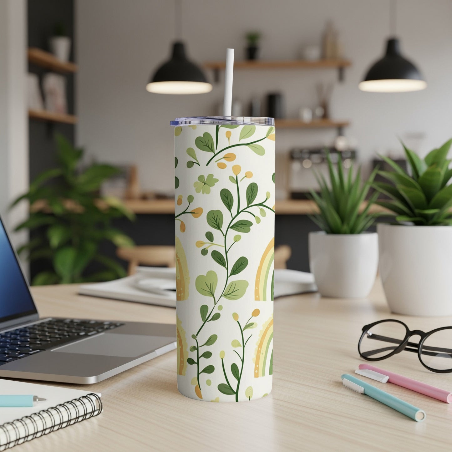 Tall tumbler with green leaves, yellow flowers, and rainbows, resting on a desk.