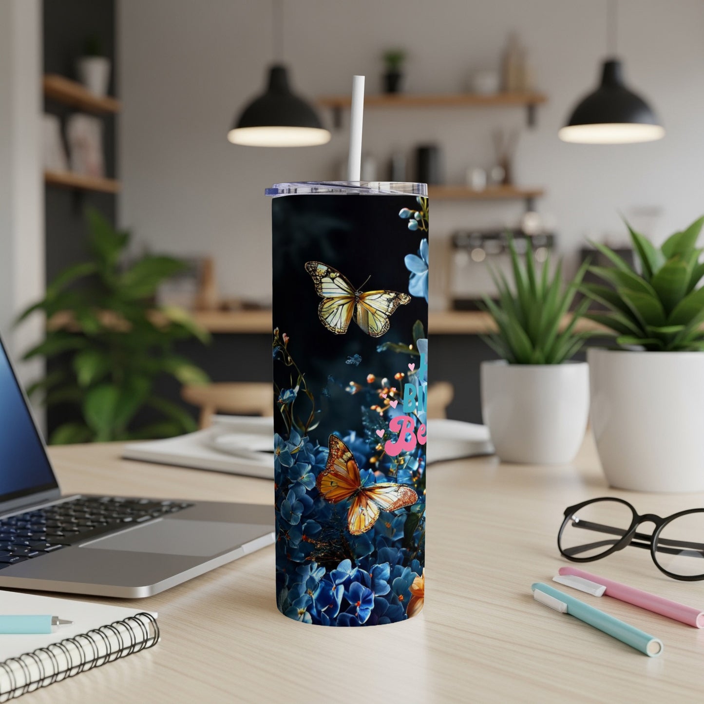 Tumbler with butterflies and pink flowers on a desk with a laptop.