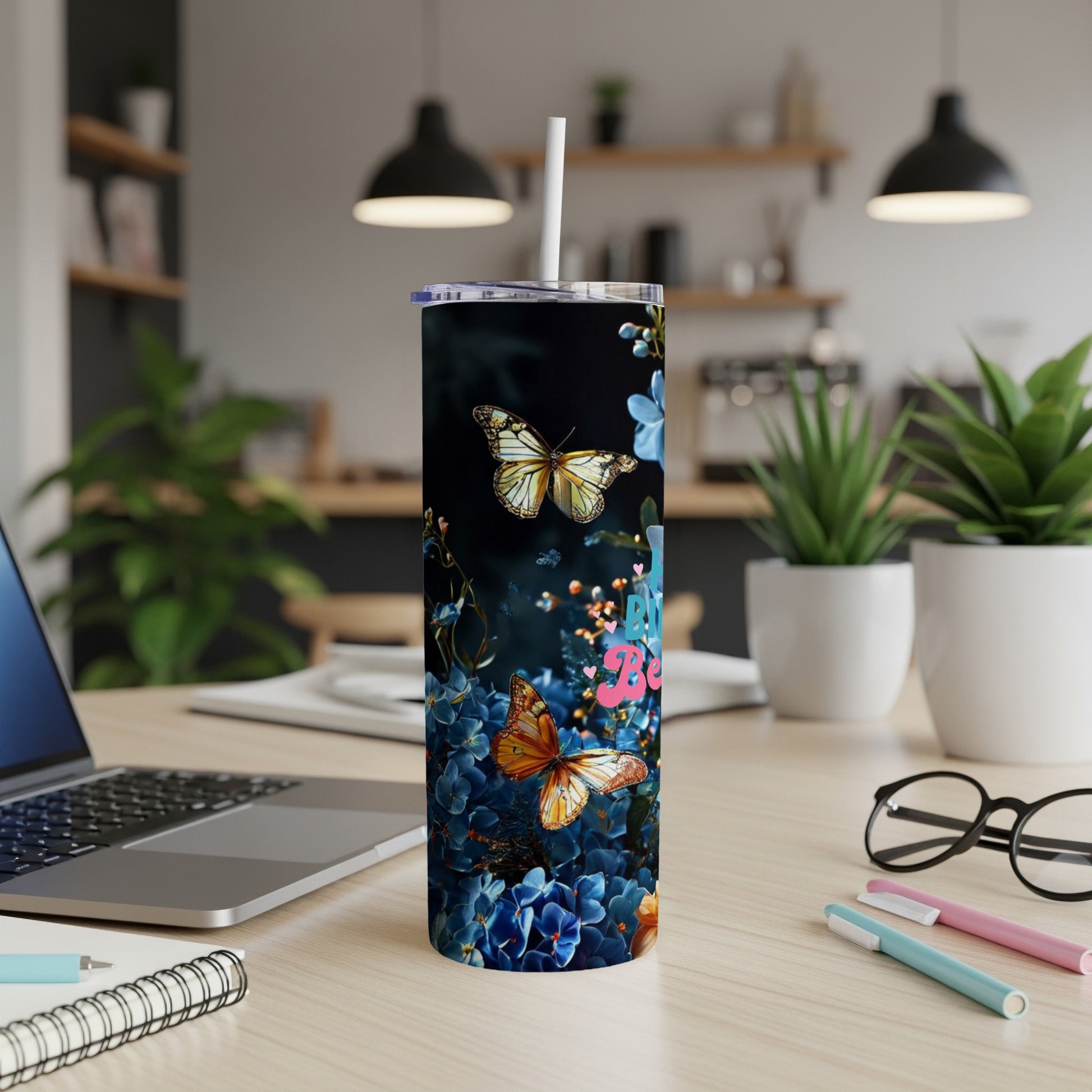 Tumbler with butterflies and pink flowers on a desk with a laptop.
