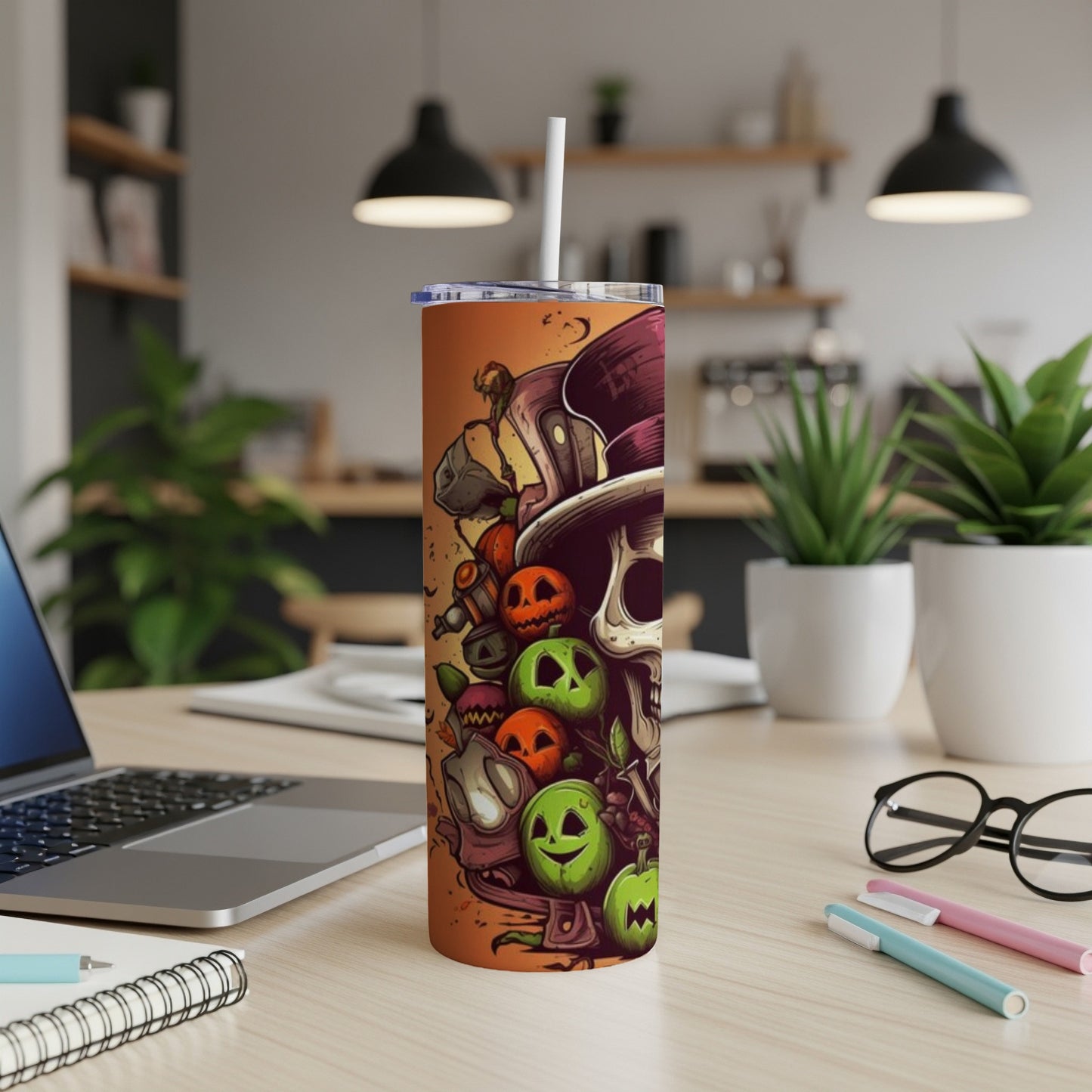 Tall tumbler with Halloween skull and pumpkin graphic, on a desk with laptop.