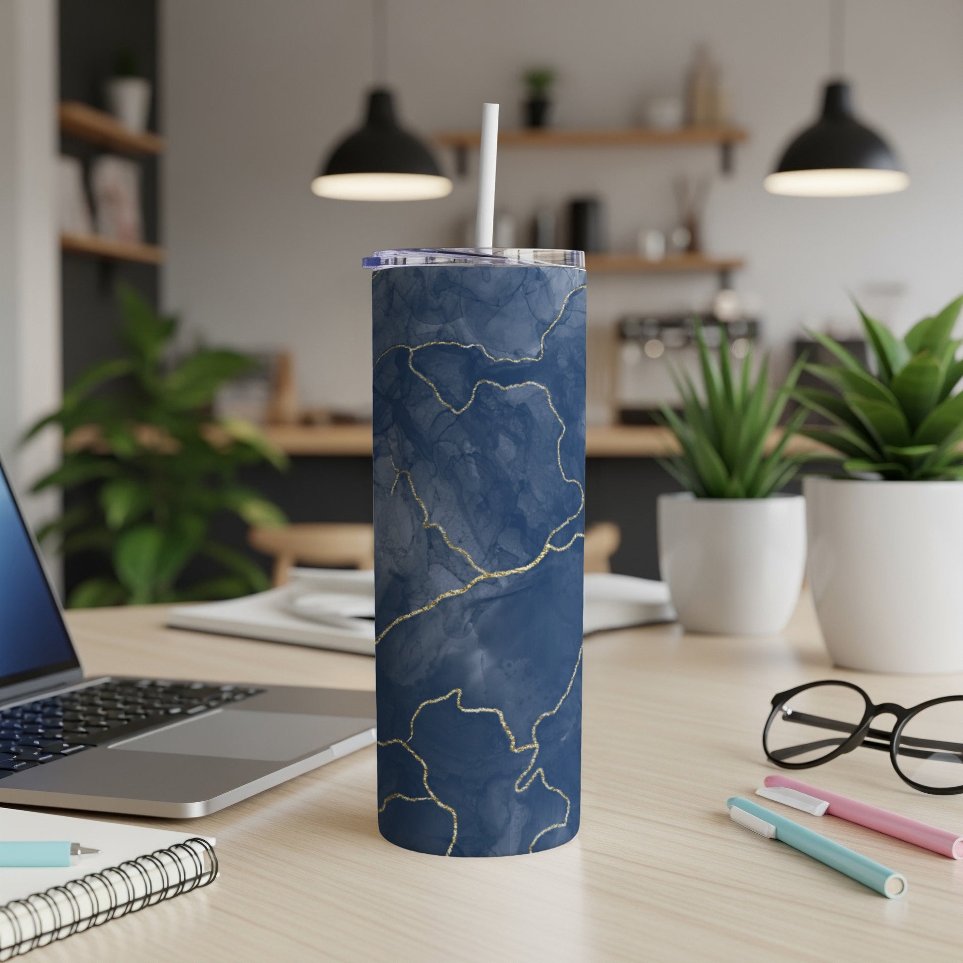 Blue marble tumbler with gold veins and straw on a desk.