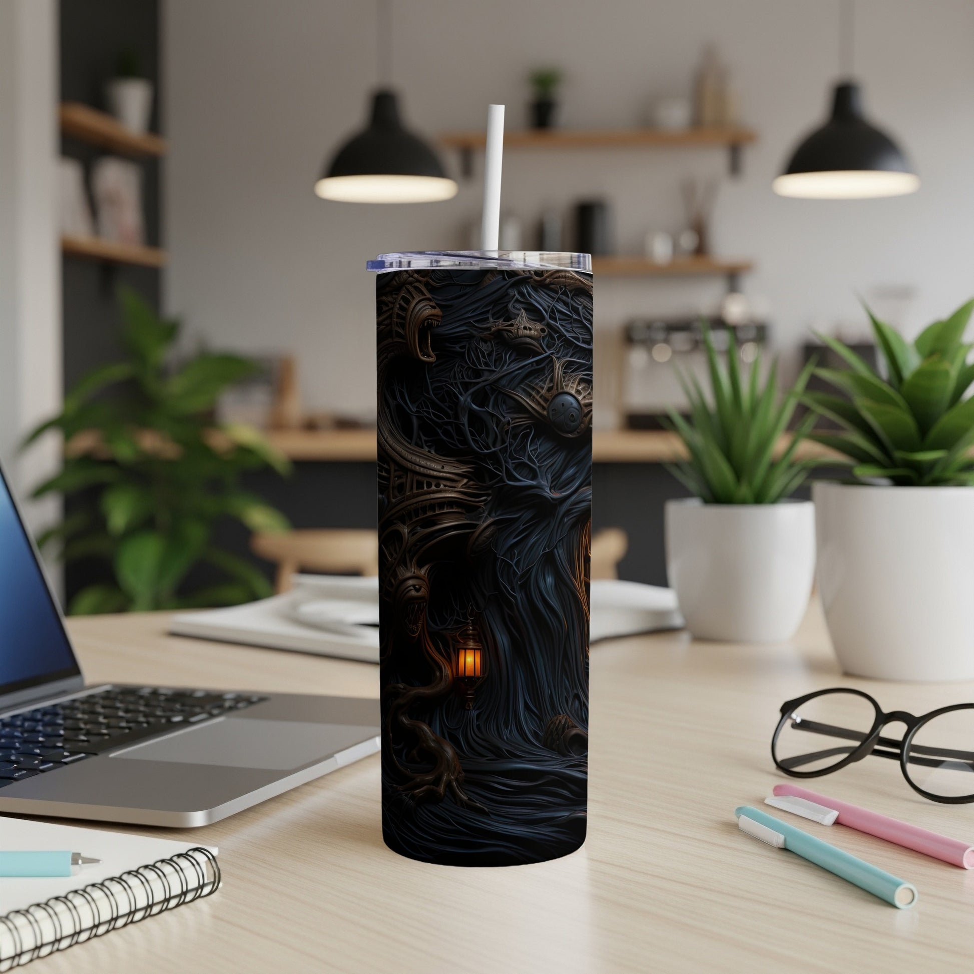 Tumbler with dark, intricate, gothic design and a straw, on a desk.