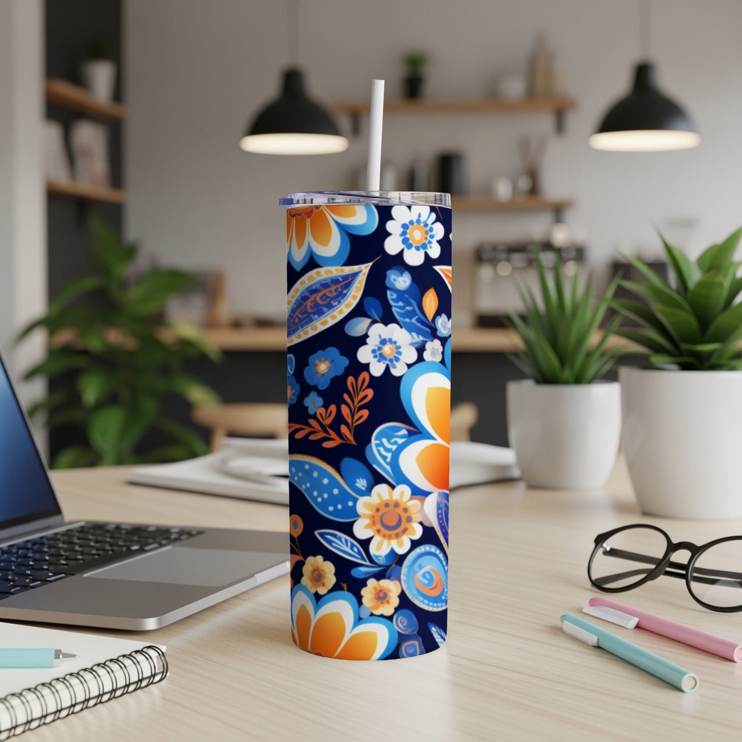 Blue and orange floral patterned tumbler with straw on desk.
