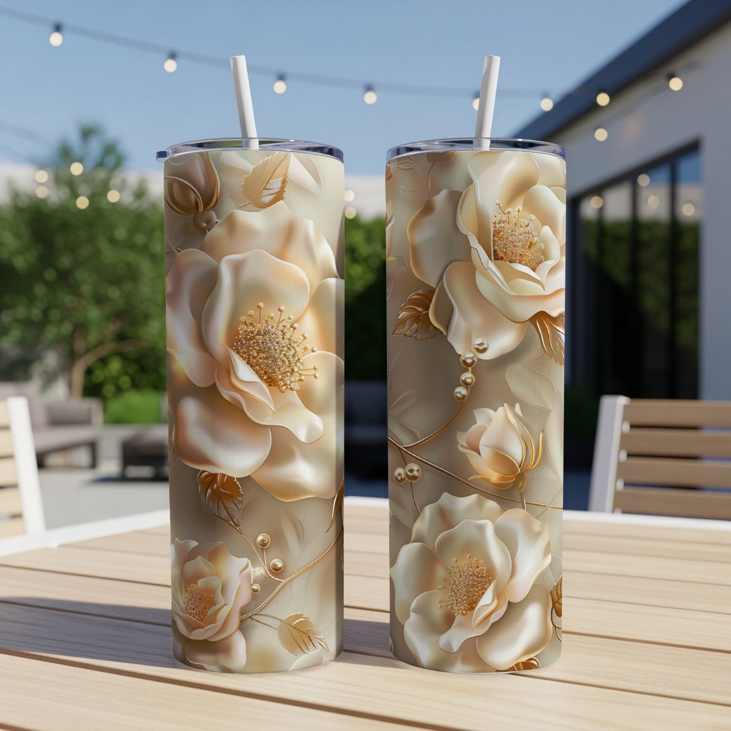 Two cream-colored rose-patterned tumblers with straws on a wooden table outdoors.