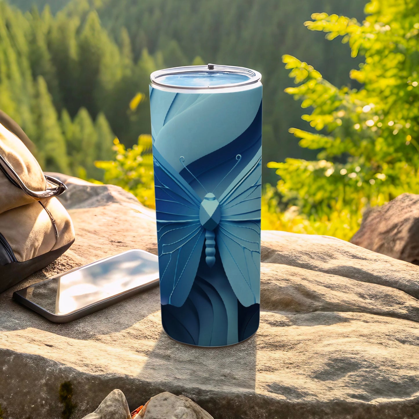 Blue butterfly design on a tumbler next to a phone and bag outdoors.