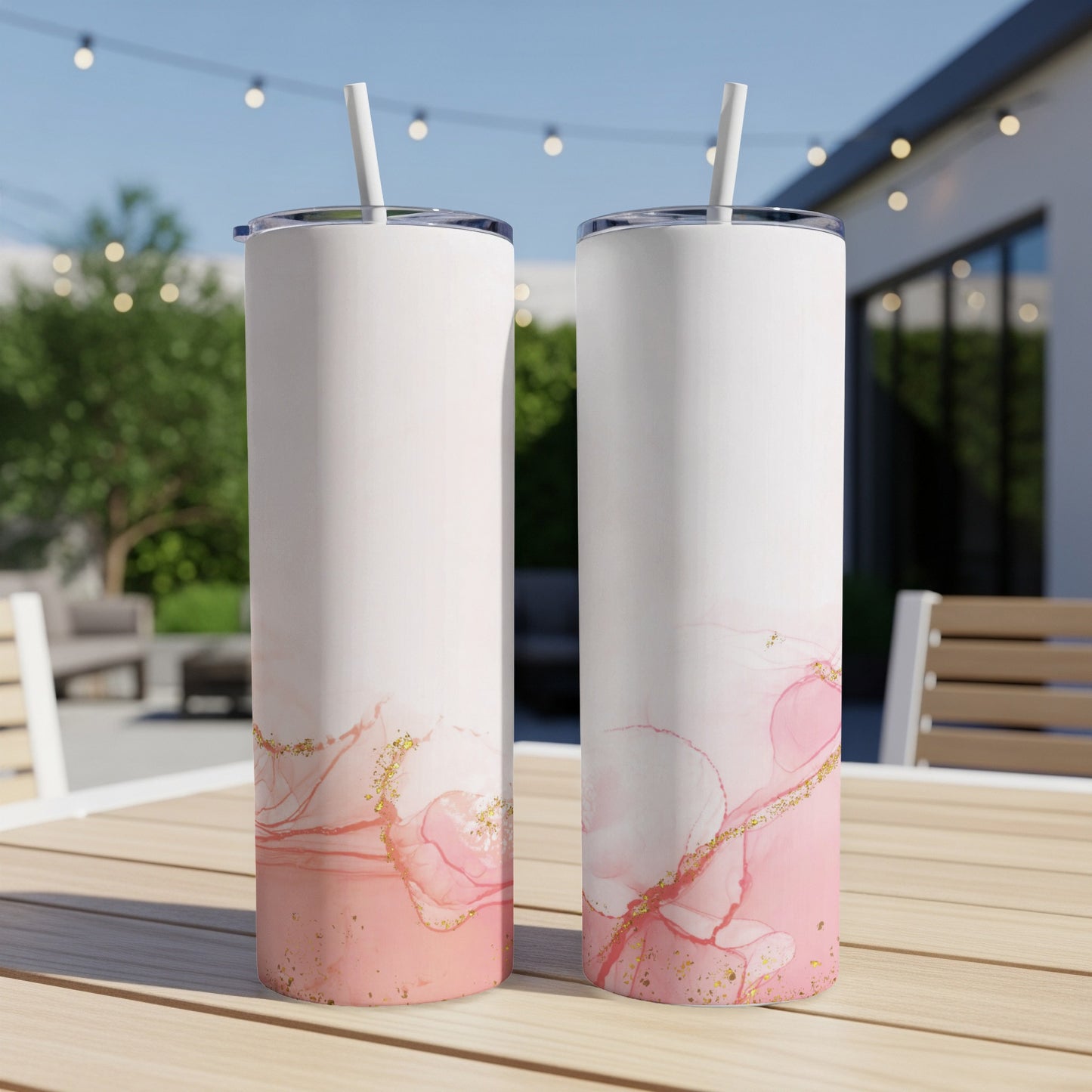 Two white tumblers with pink watercolor and gold splatter design on a wooden table.