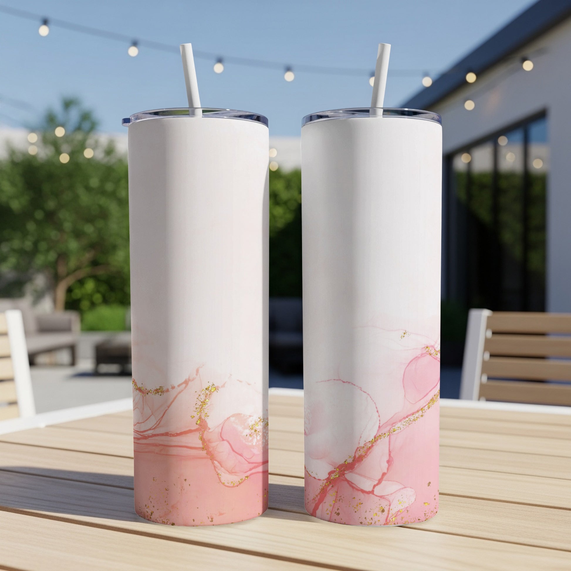 Two white tumblers with pink watercolor and gold splatter design on a wooden table.