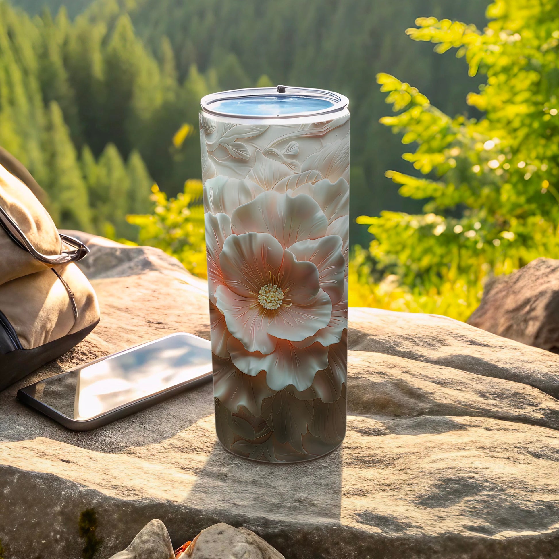 Floral tumbler with textured petals rests on rock with phone and backpack.