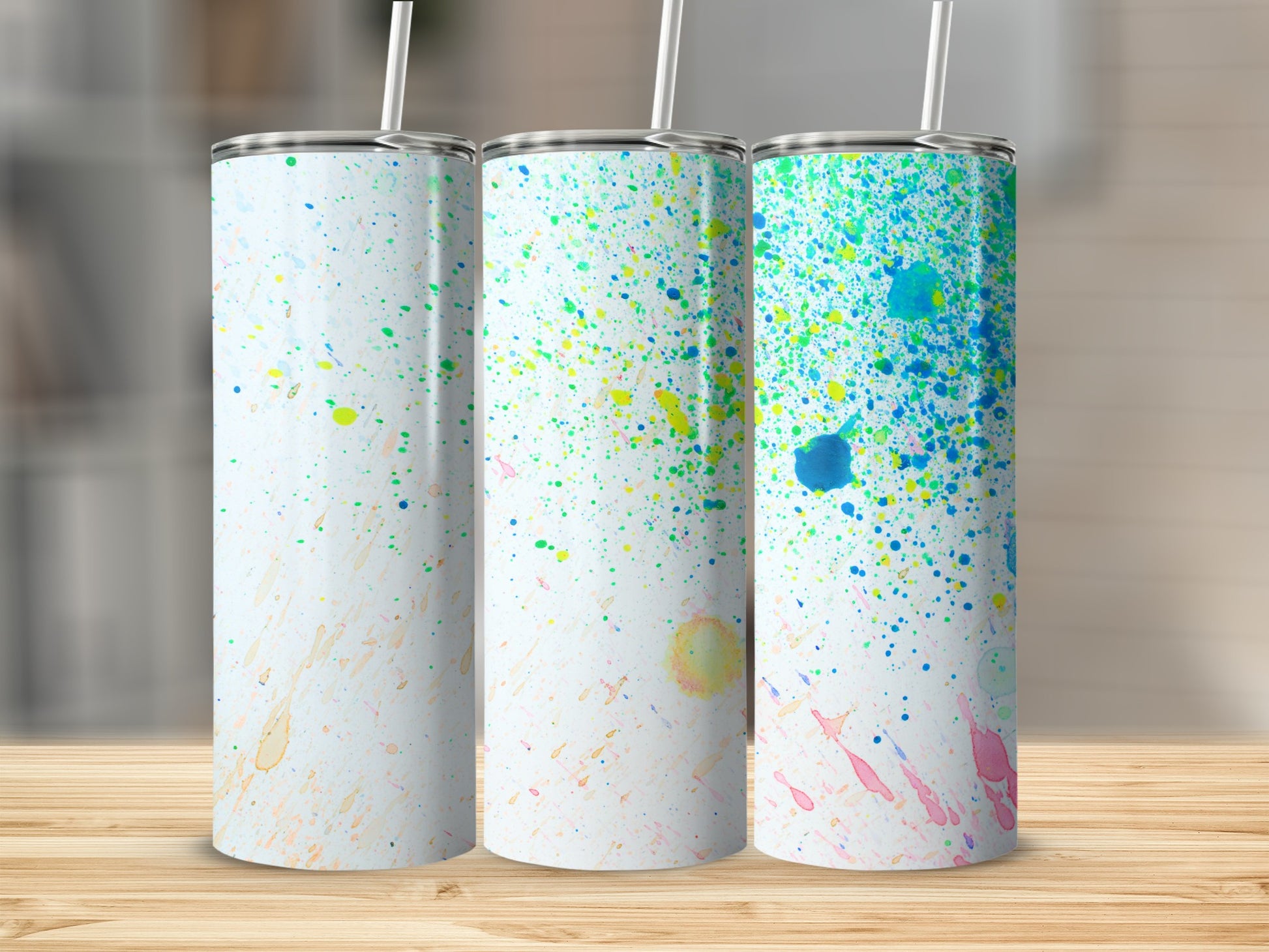 Three white tumblers with colorful paint splatters, arranged on a wooden surface.