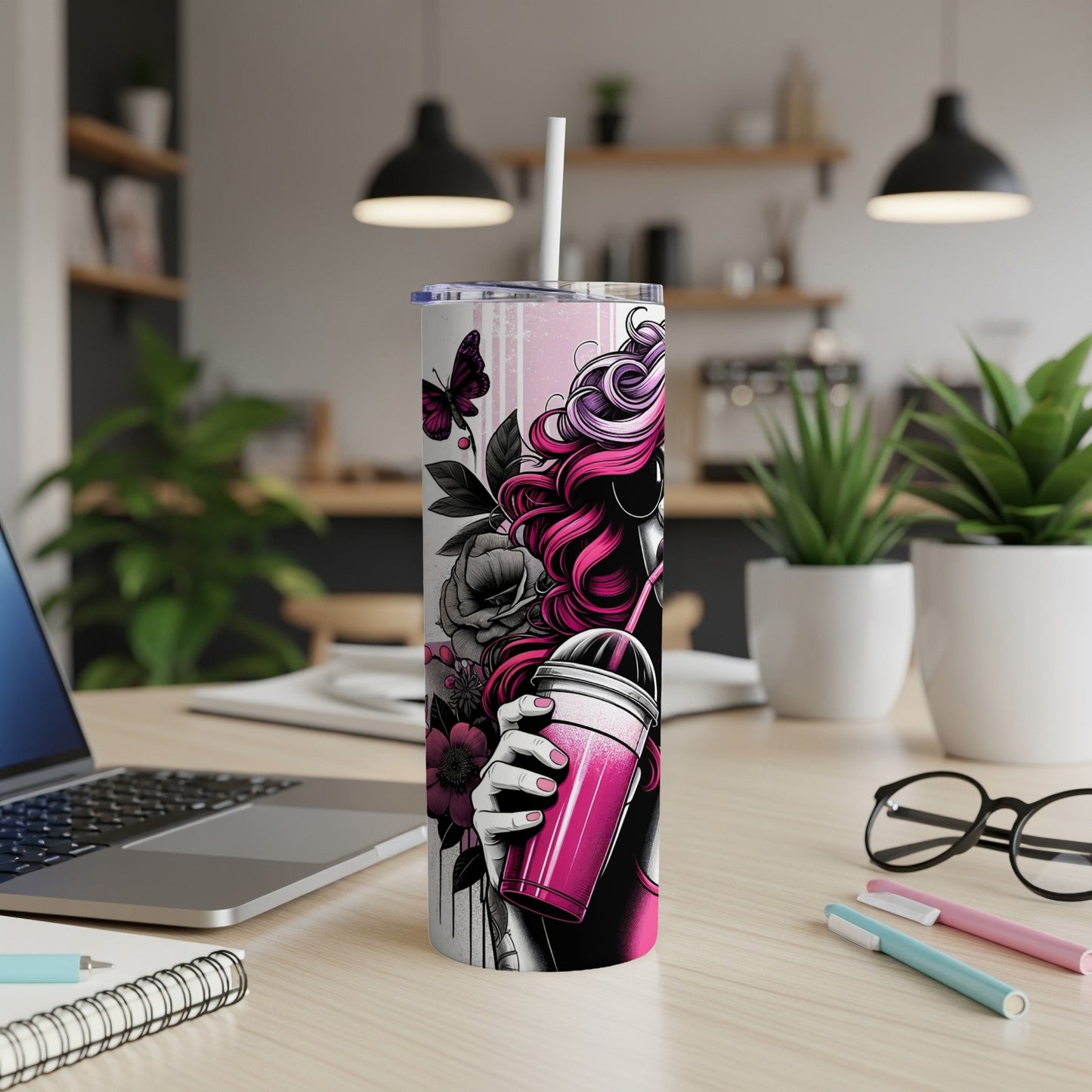 Pink tumbler with woman's silhouette and flowers, on desk with laptop.