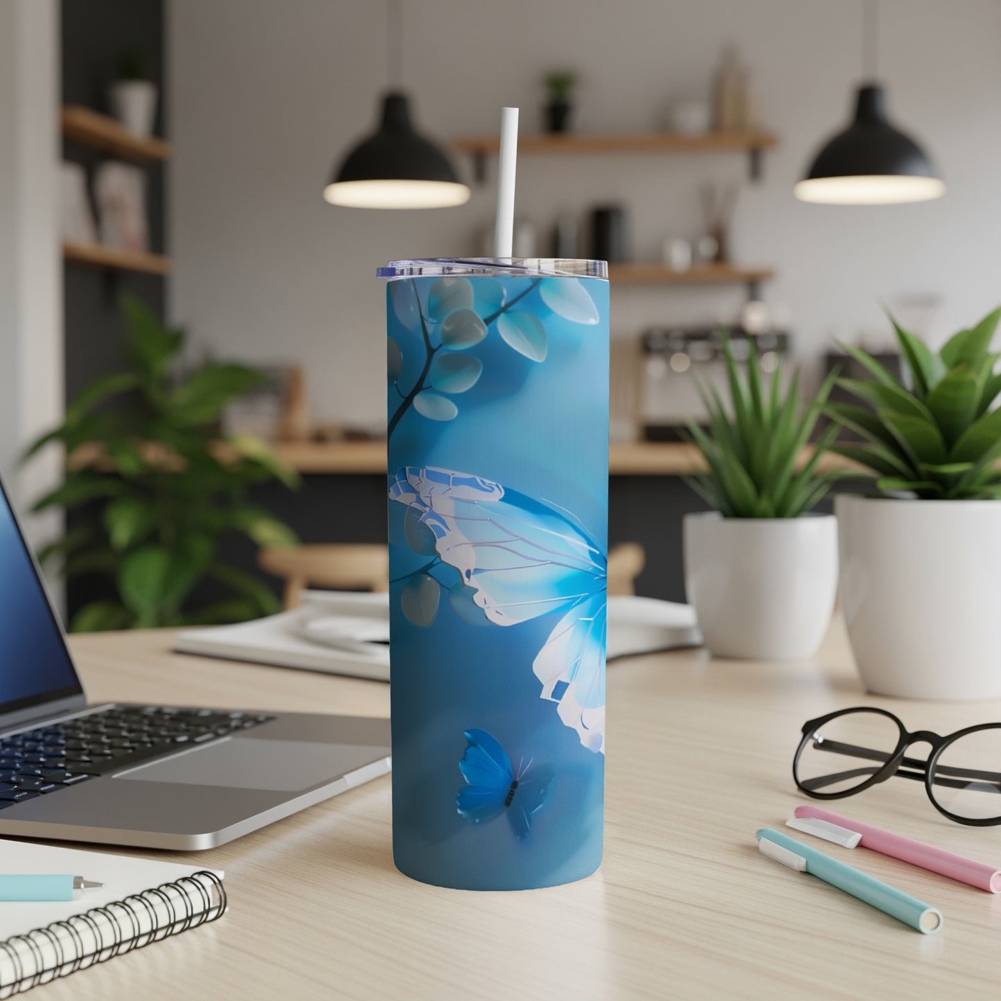 Blue butterfly tumbler with straw on a desk with a laptop and pens.