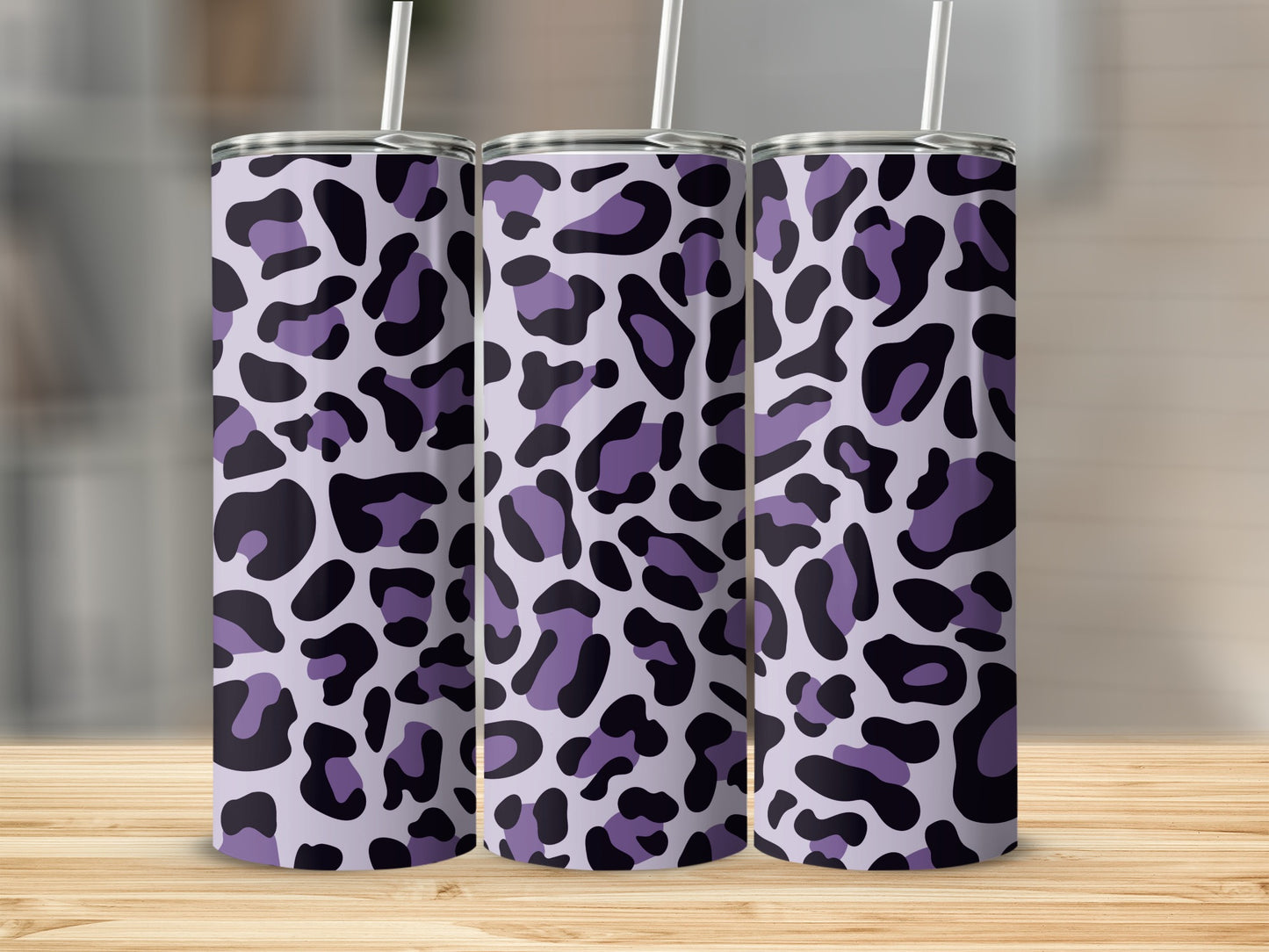 Three purple leopard print tumblers with straws on a wooden surface.