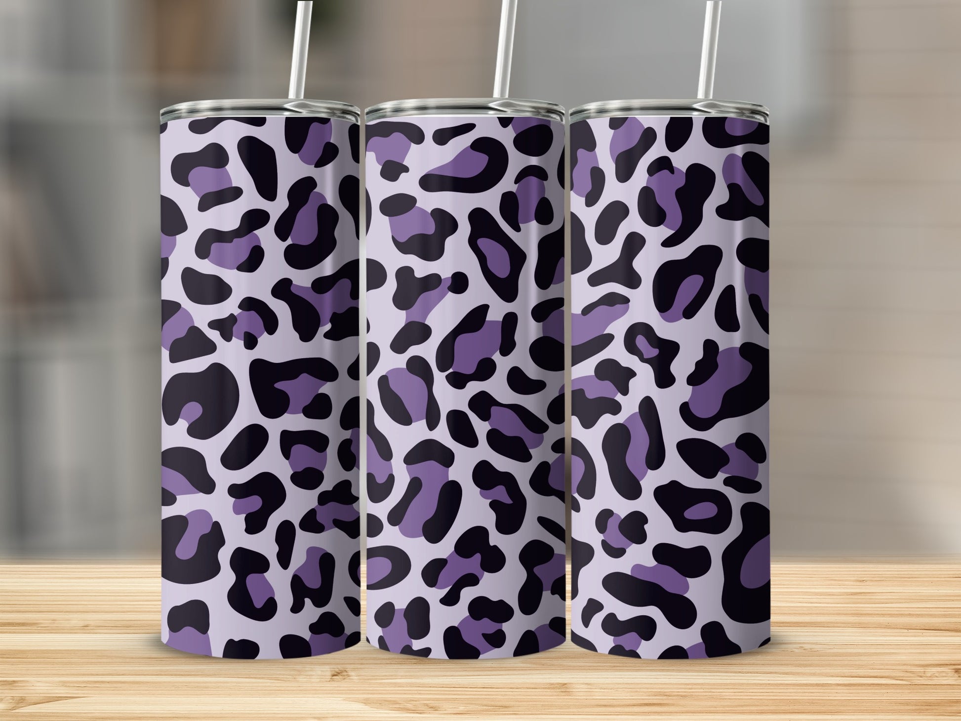 Three purple leopard print tumblers with straws on a wooden surface.