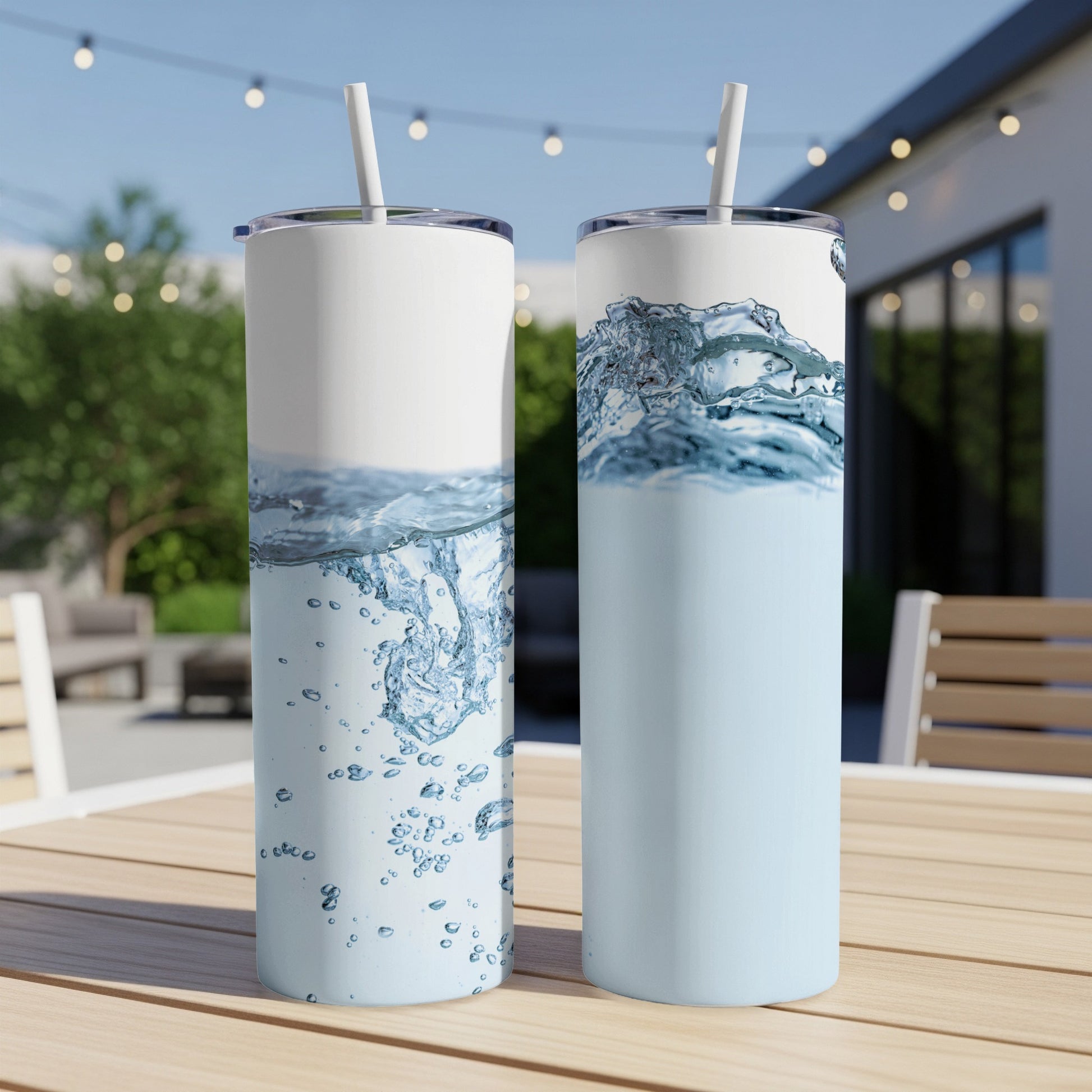 Two tall tumblers with water and blue liquid, on a wooden table outdoors.