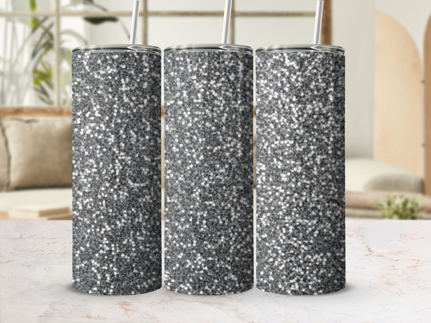 Three silver glitter tumblers with straws displayed on a marble surface.