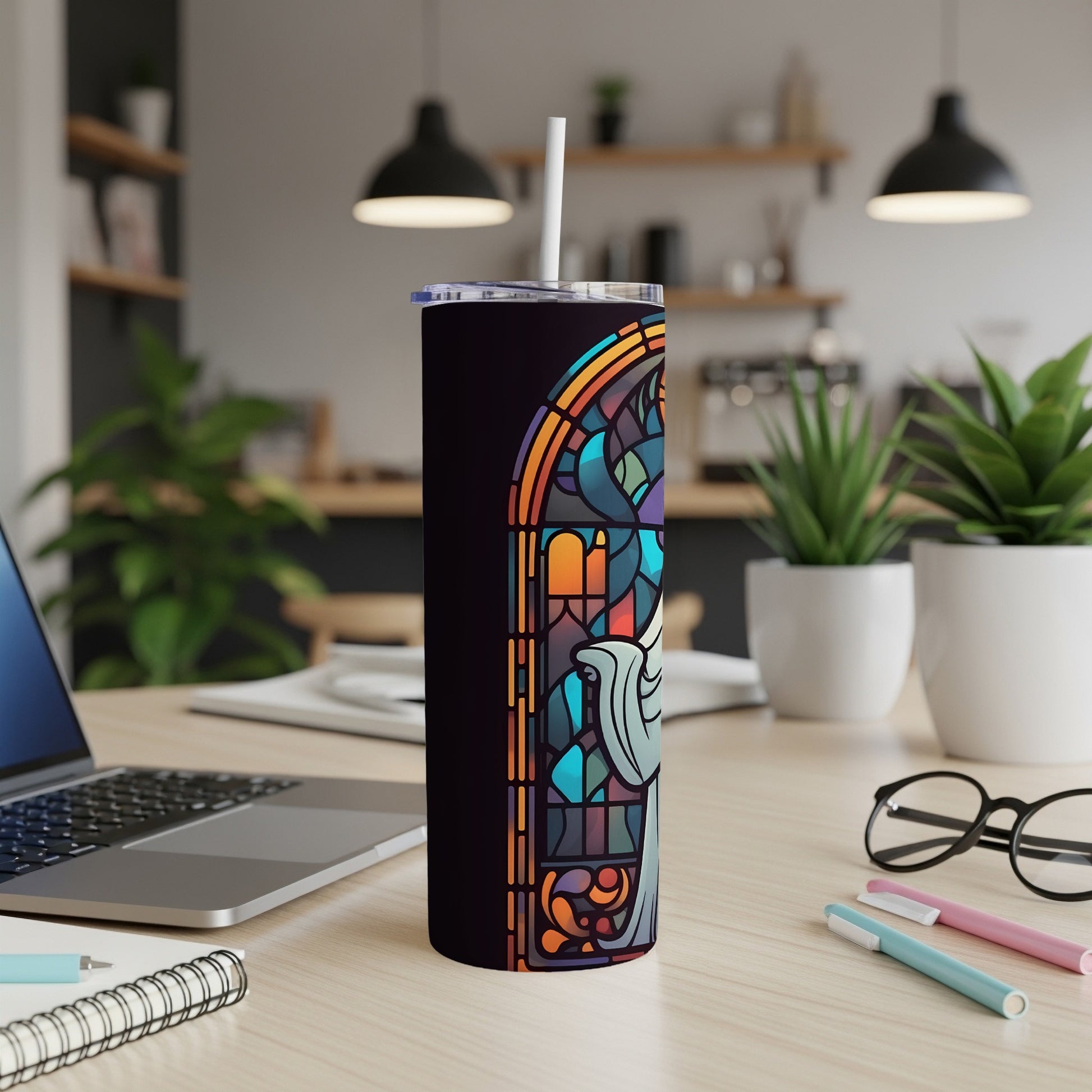 Stained glass tumbler with angel design and straw on a desk.