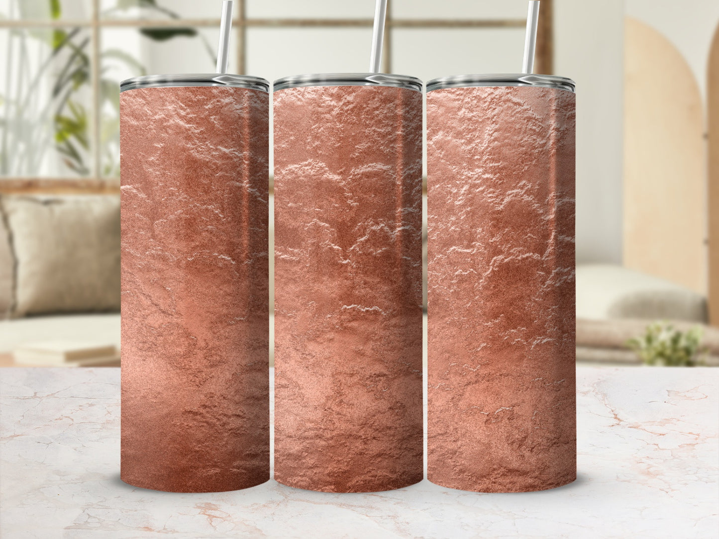 Three rose gold textured tumblers with silver lids and straws on a marble surface.