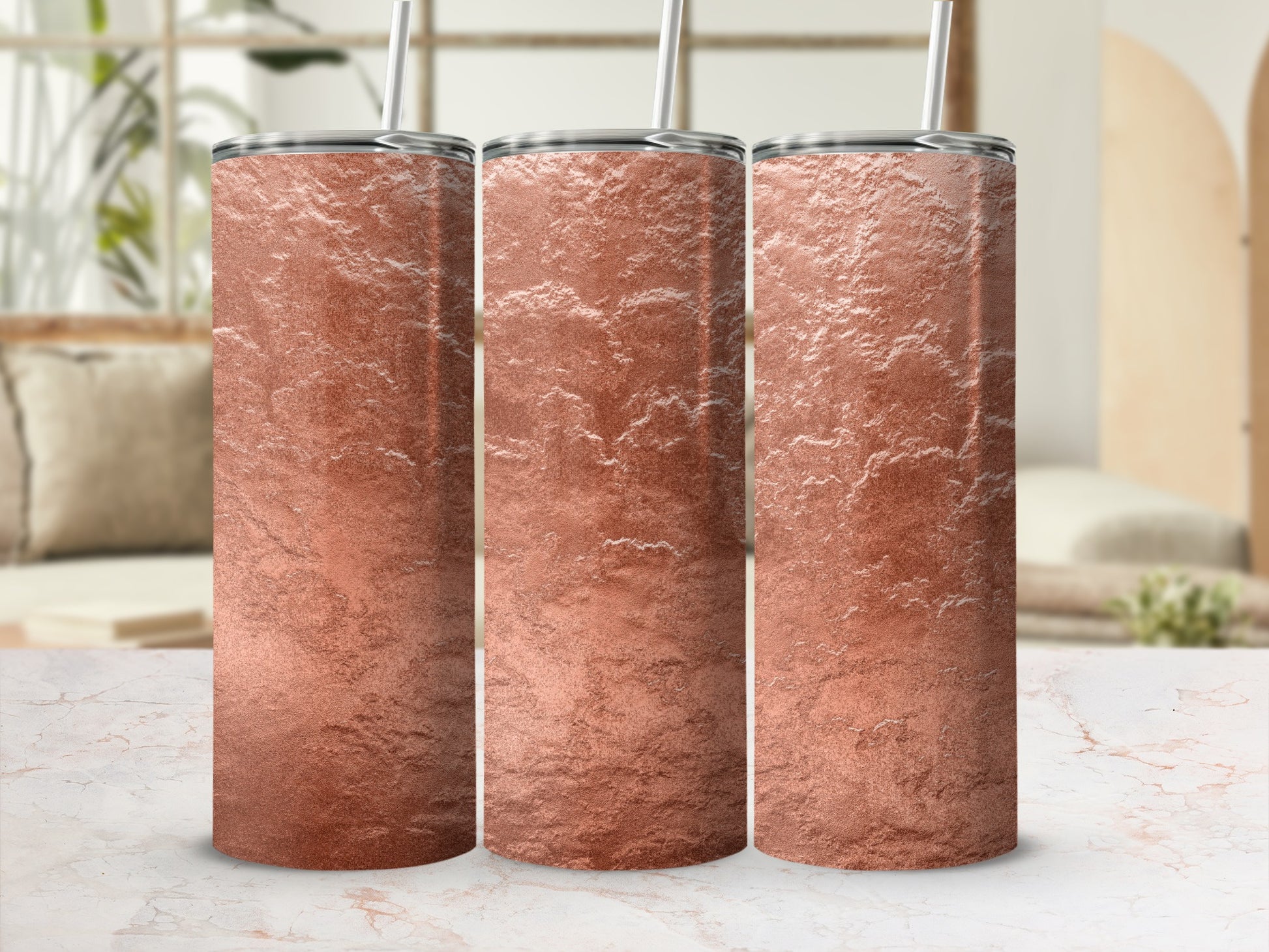 Three rose gold textured tumblers with silver lids and straws on a marble surface.