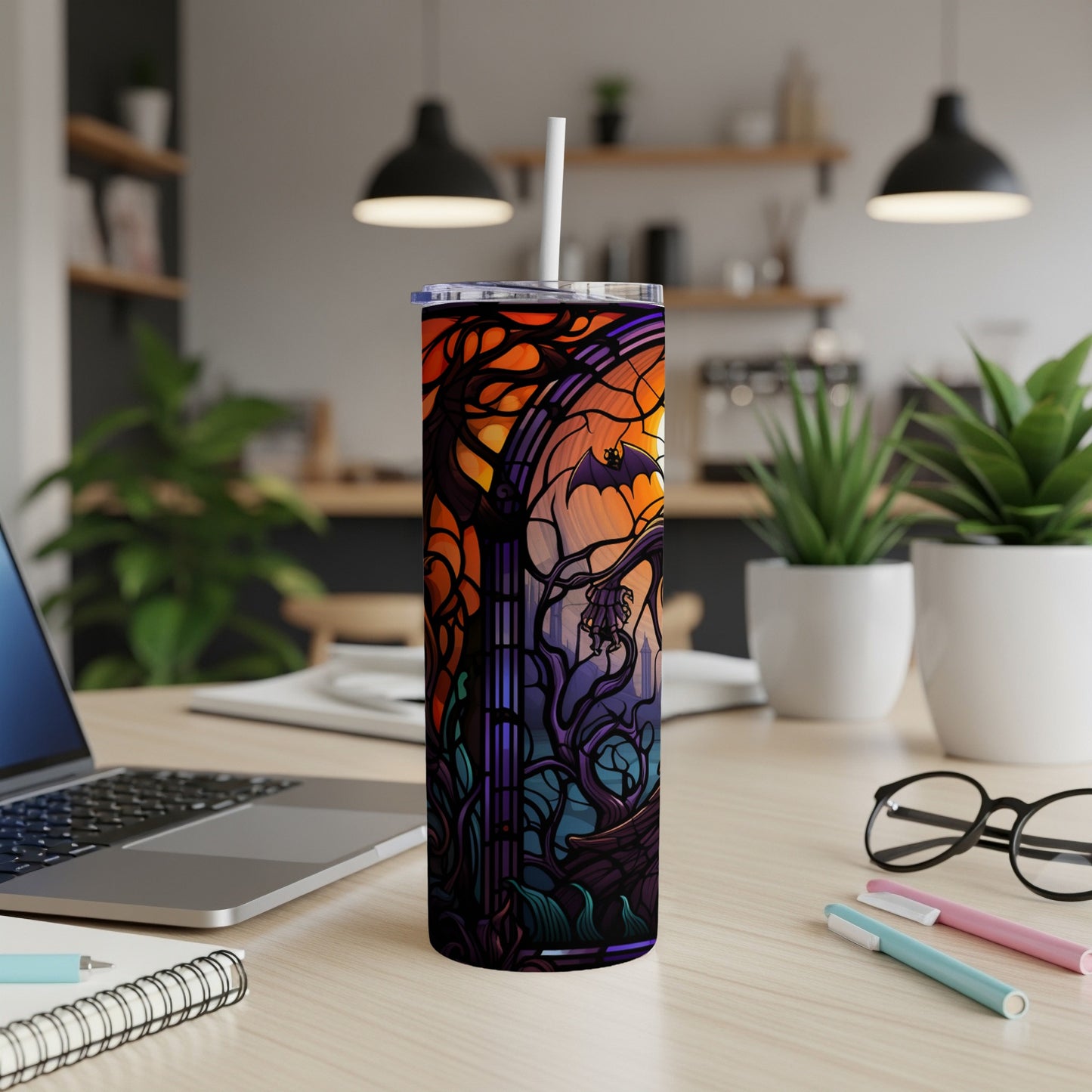 Stained glass tumbler with gothic bat design and straw, on desk.