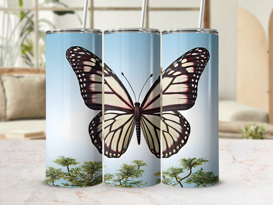 Tumbler with monarch butterfly and green foliage against a light blue sky.