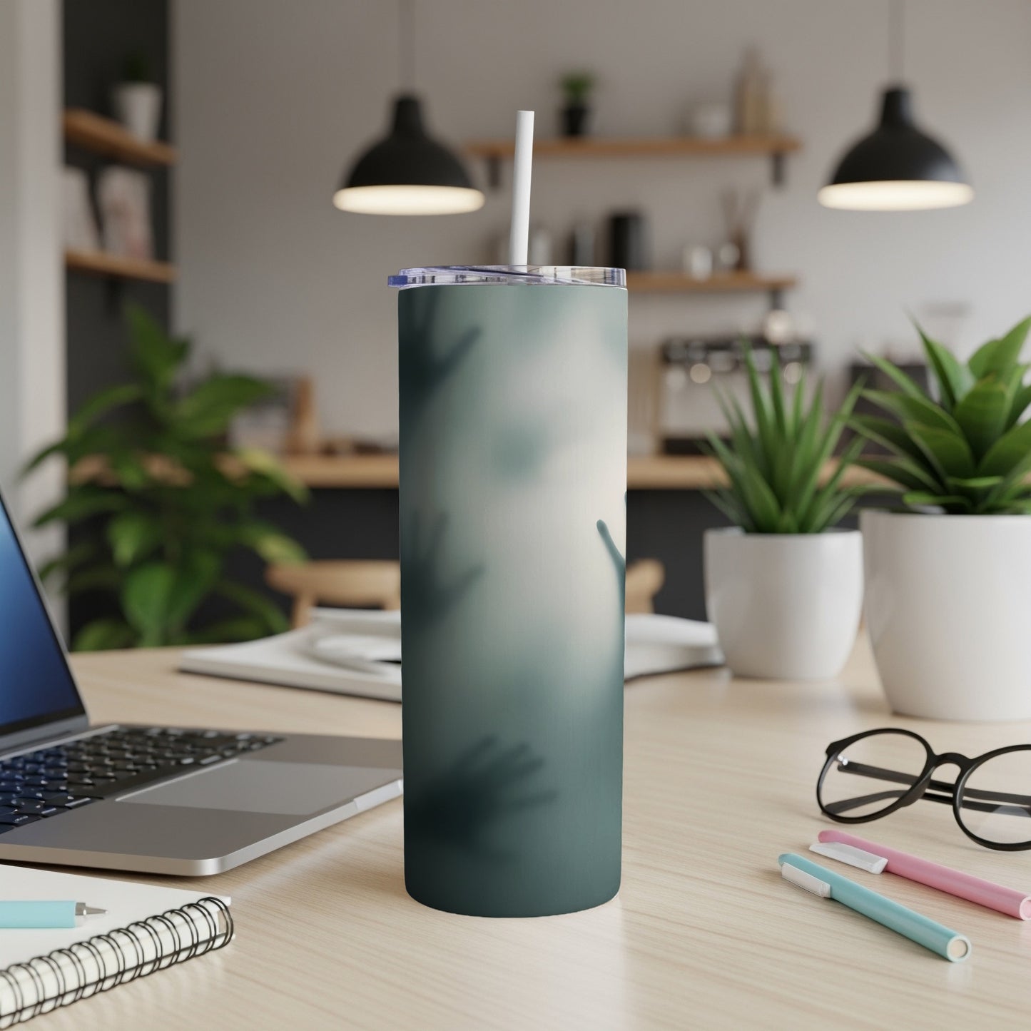 Green tumbler with hazy handprint design on a desk with laptop and plants.