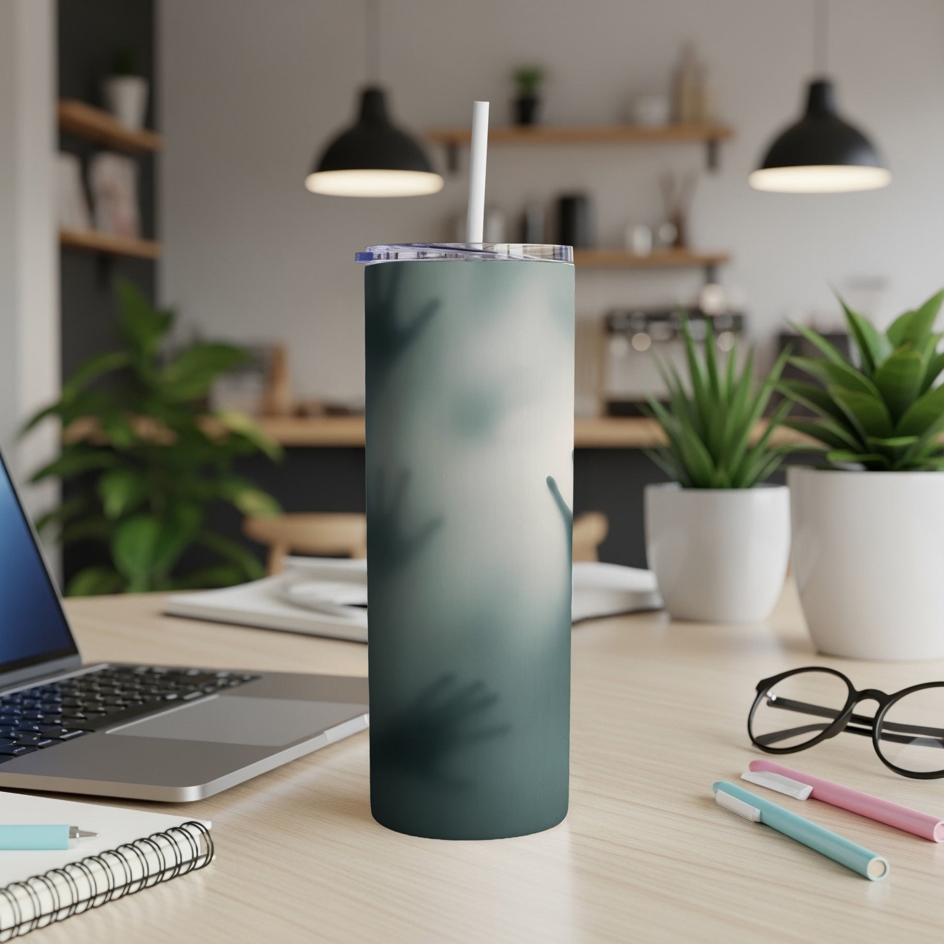 Green tumbler with hazy handprint design on a desk with laptop and plants.