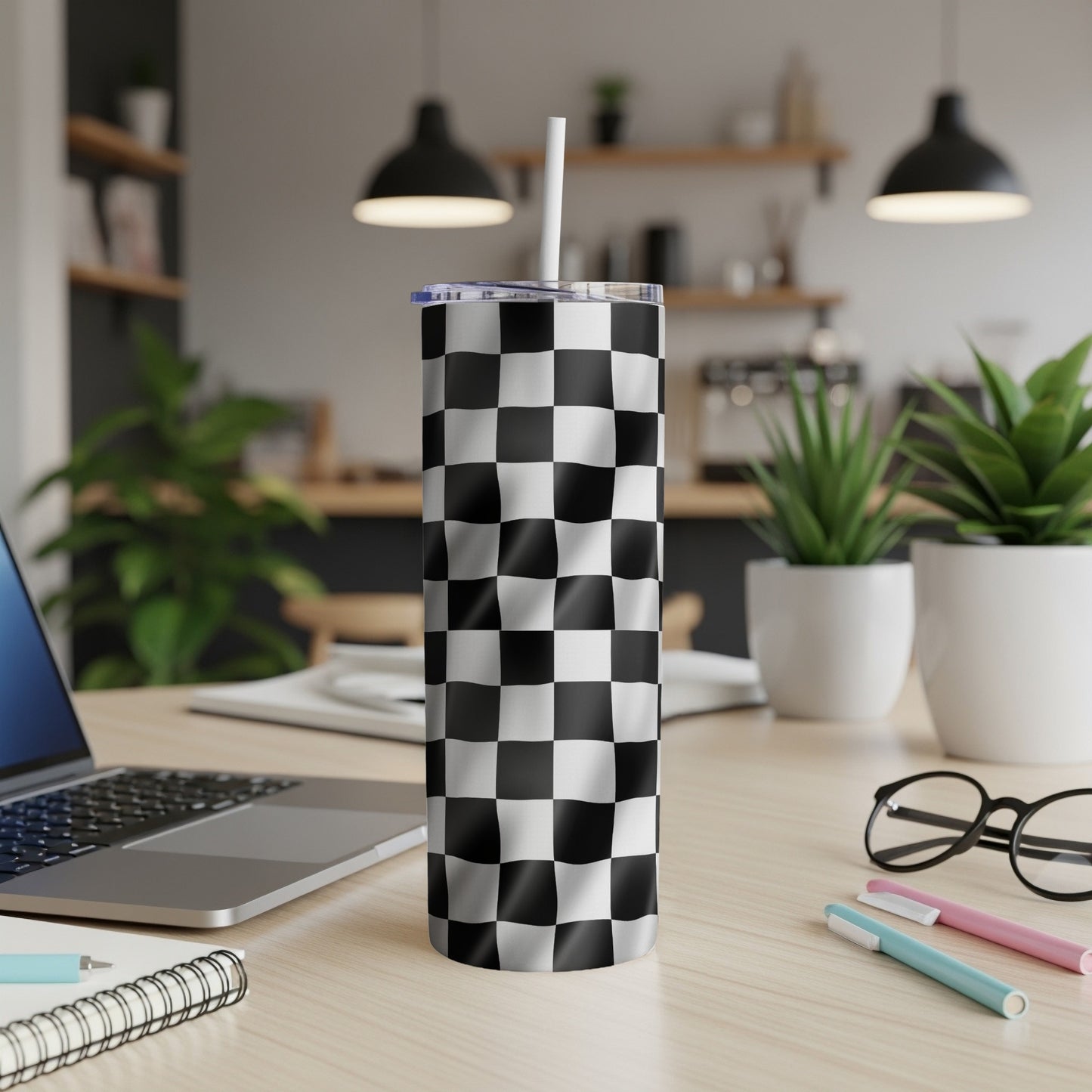 Checkerboard tumbler with a white straw on a wooden desk.