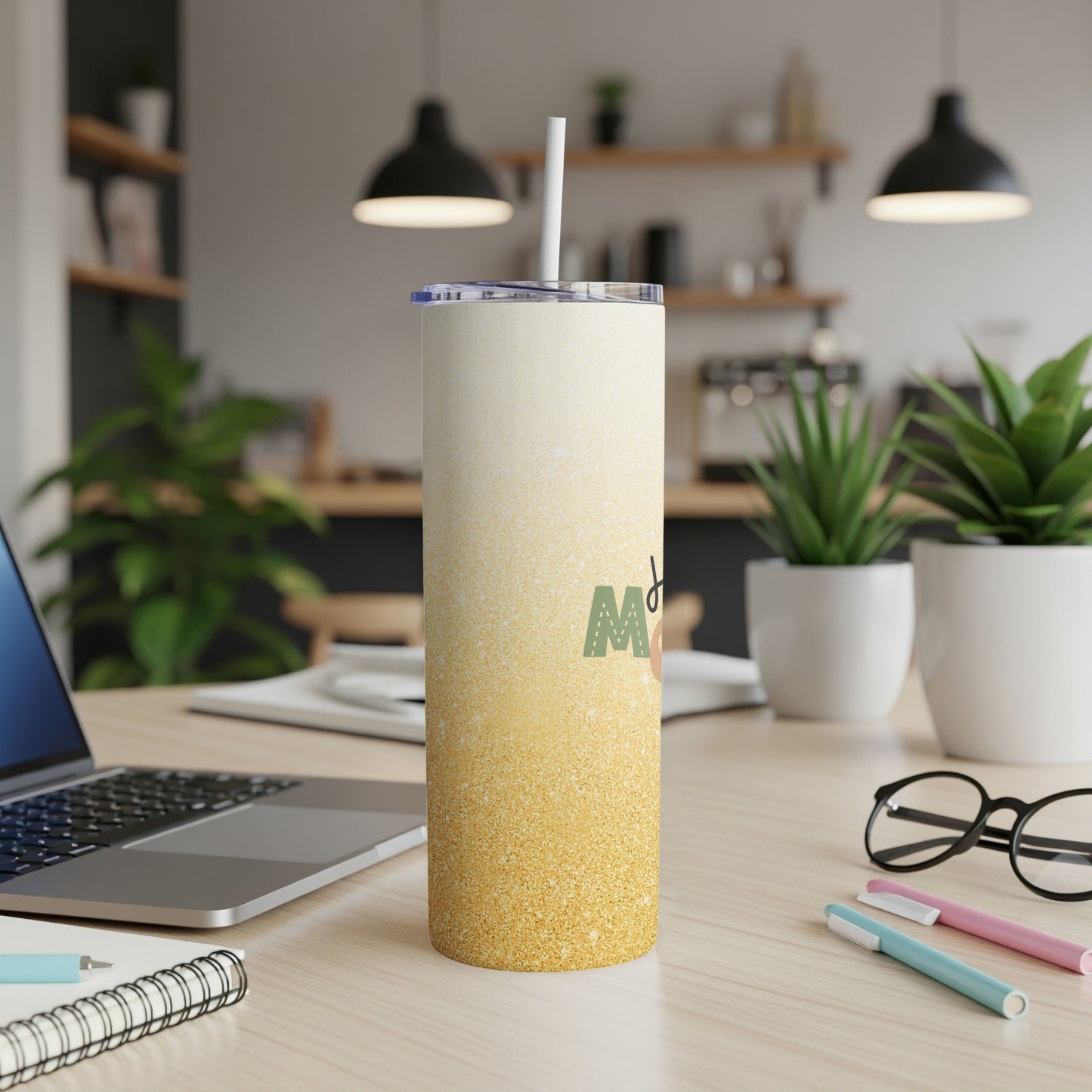 Glittery gold and white tumbler with straw, on a desk with laptop and pens.