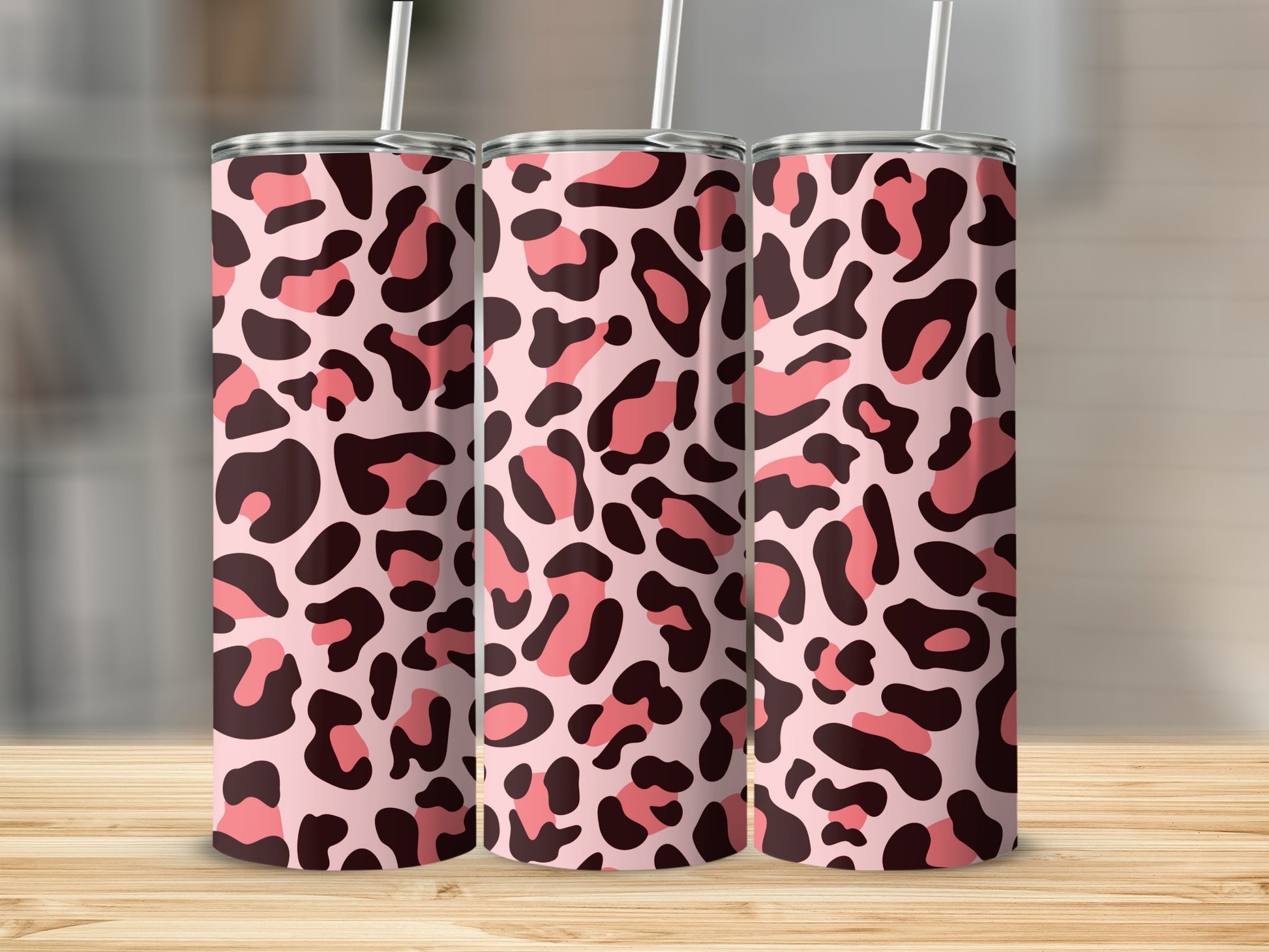 Three sleek tumblers patterned with pink and brown leopard print stand on a wooden surface.