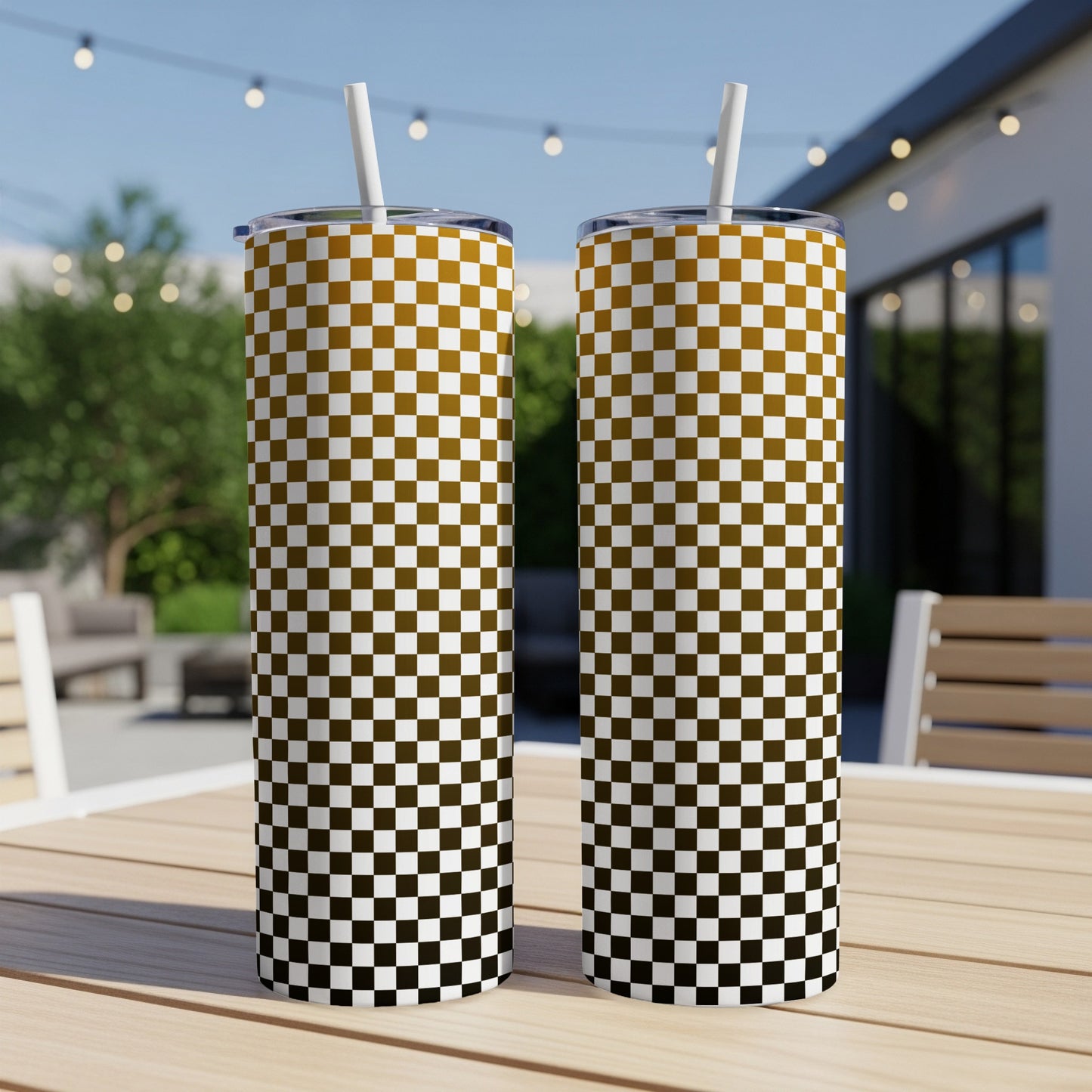 Two tall tumblers with a checkered pattern sit on a wooden table outdoors.