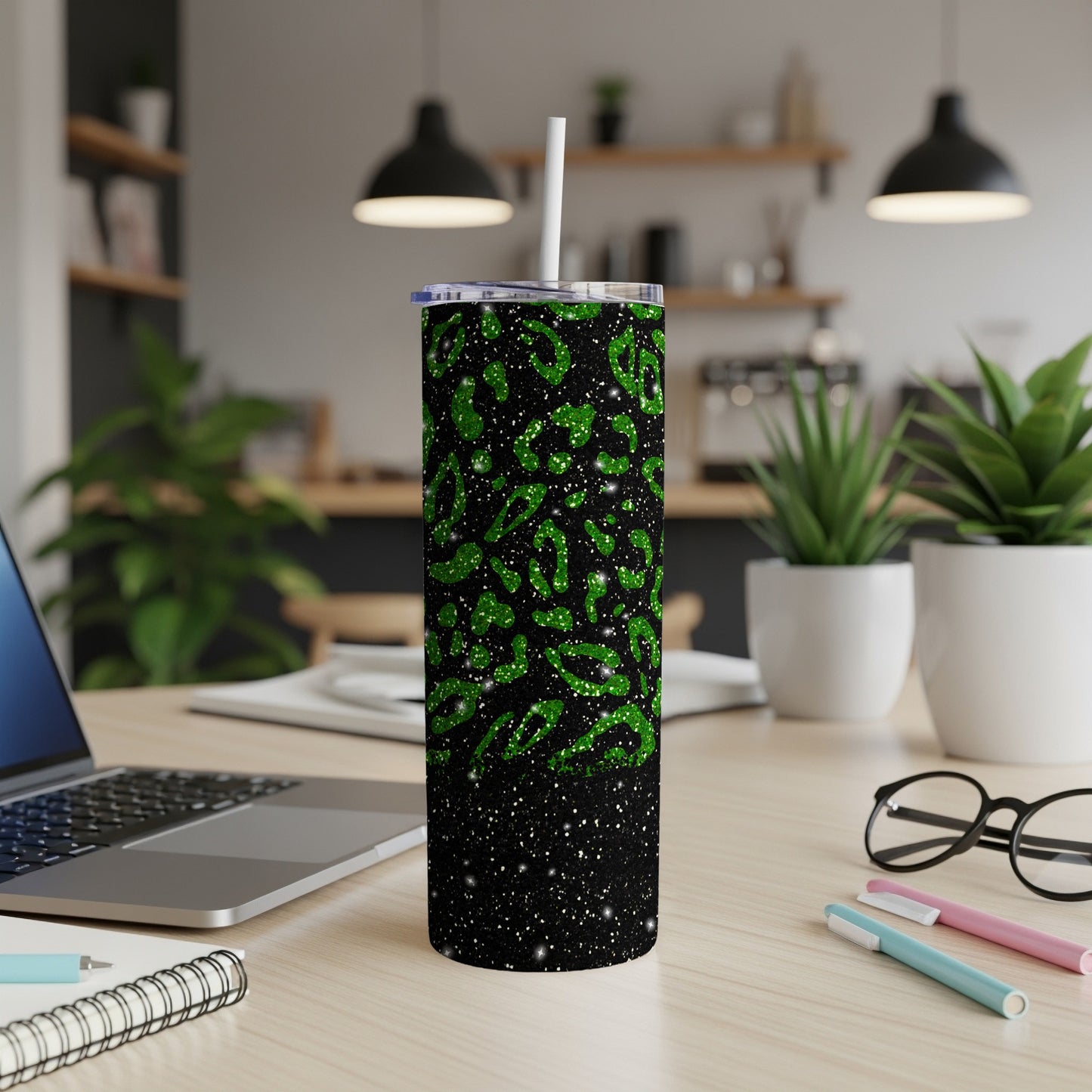 Black tumbler with green leopard print and glitter, on a desk.
