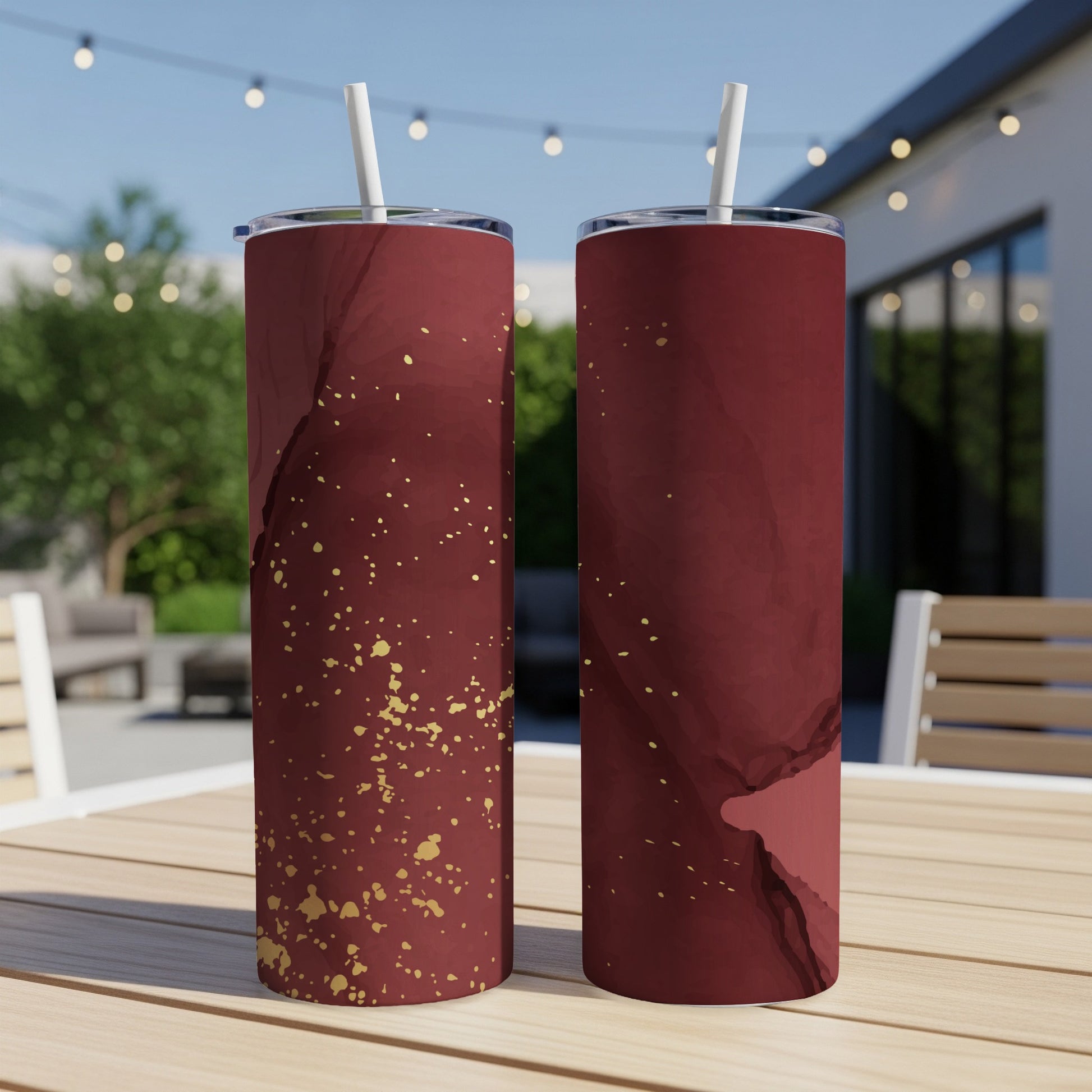 Two maroon tumblers with gold splatter and marble design on a table.