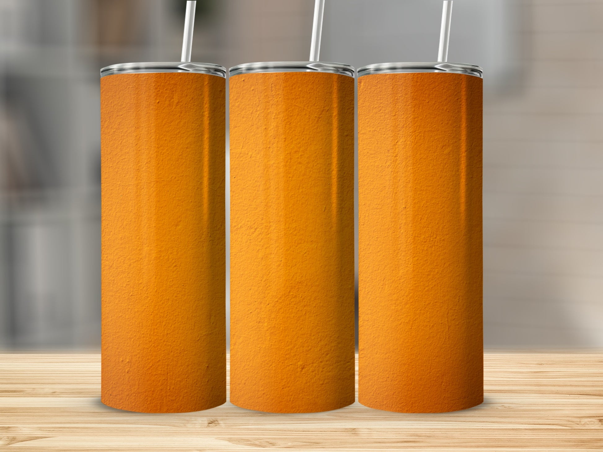 Three tall orange tumblers with white straws on a wooden surface.