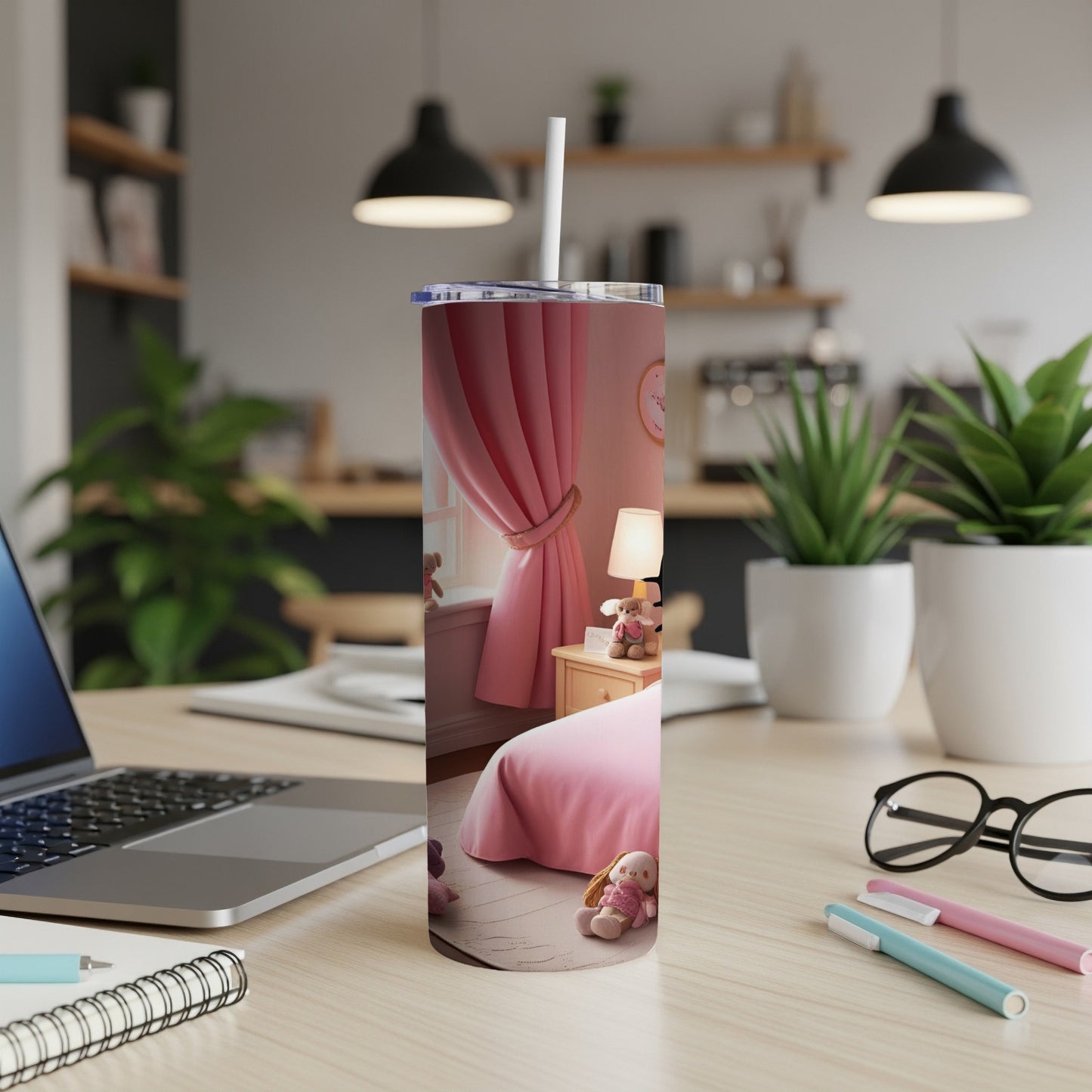 Pink tumbler with cartoon animals on a desk next to a laptop and pens.