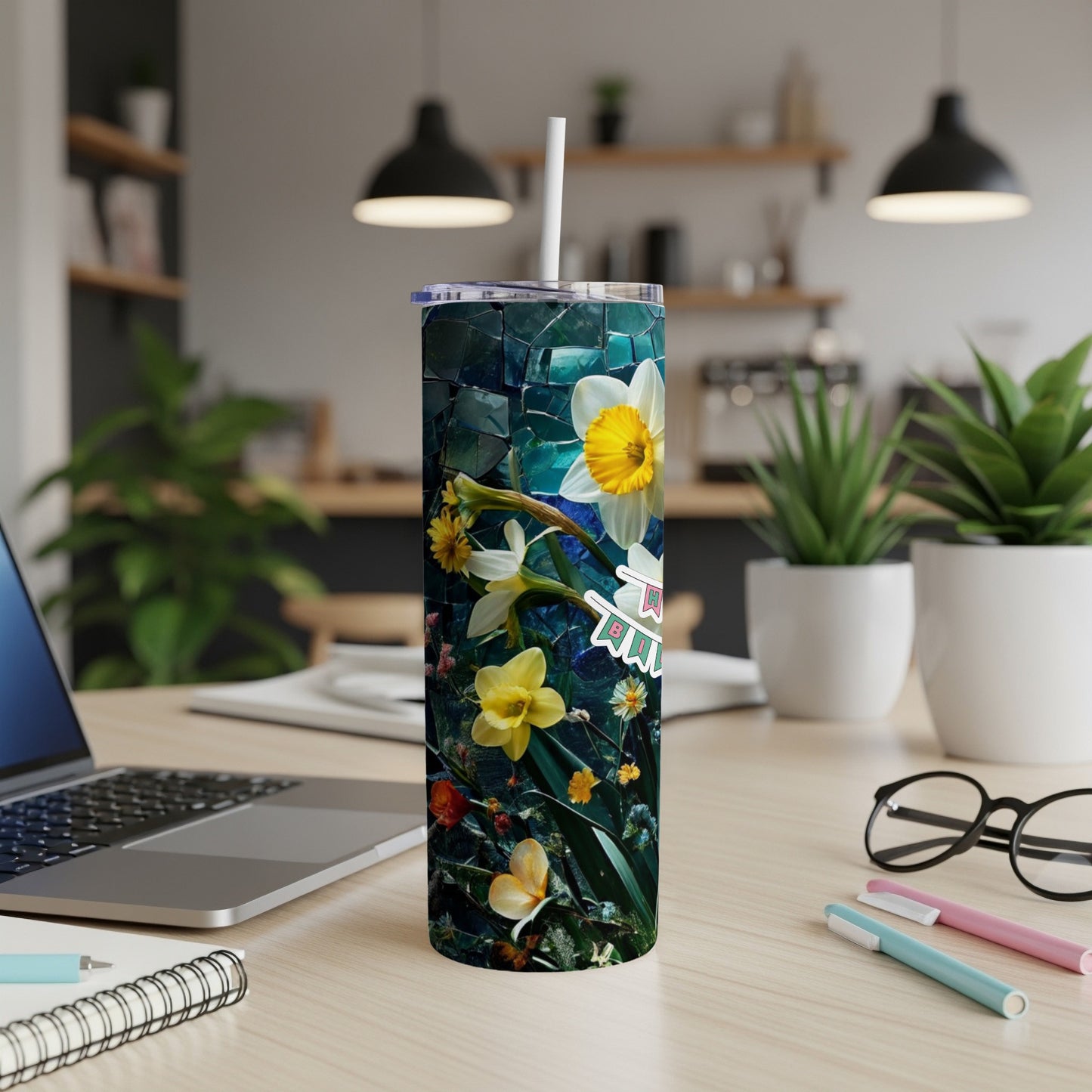 Daffodil and floral patterned tumbler with a straw, on a desk.