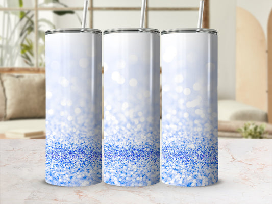 Three white tumblers with blue glitter gradient and straw on marble countertop.