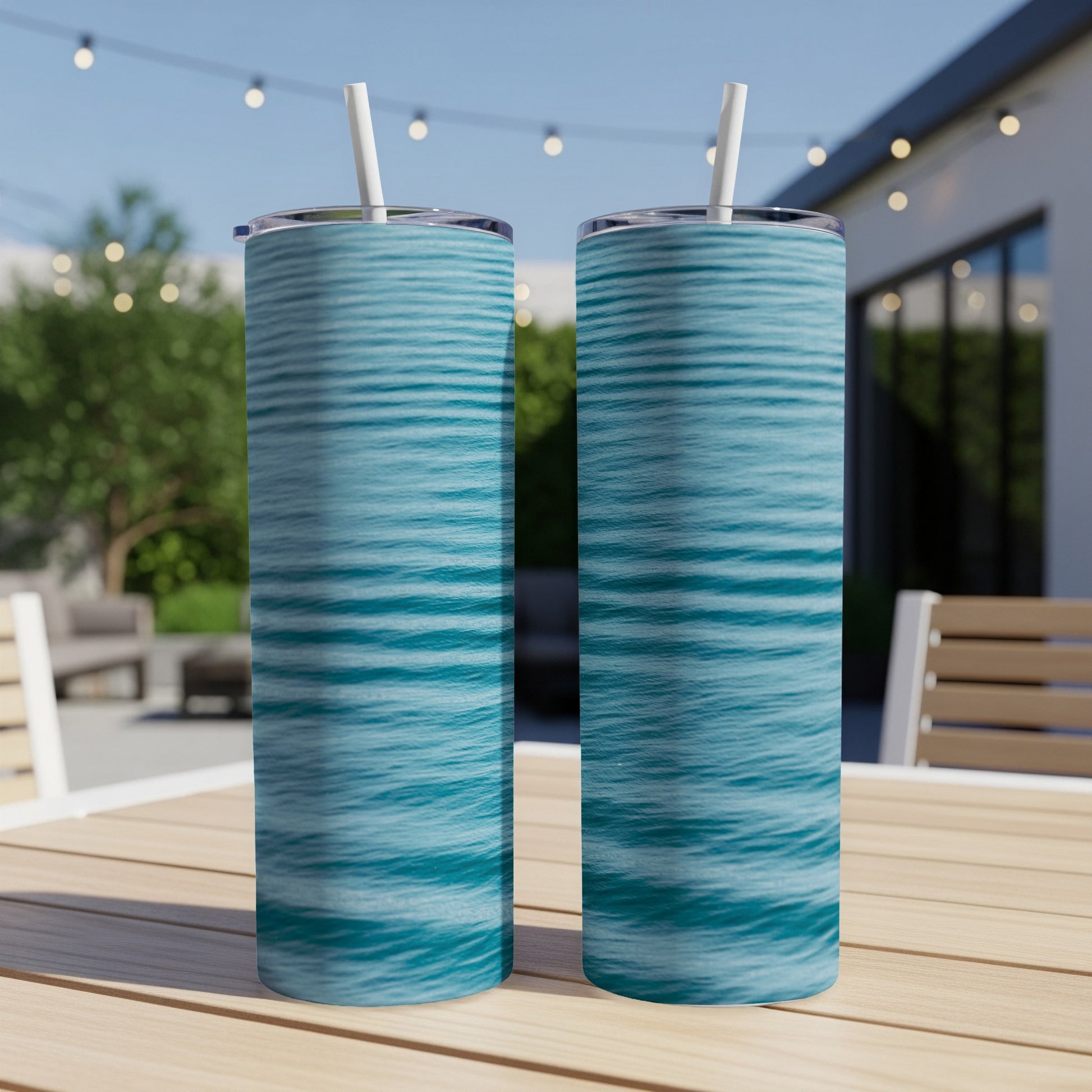 Two blue and teal striped tumblers with straws on a wooden table.