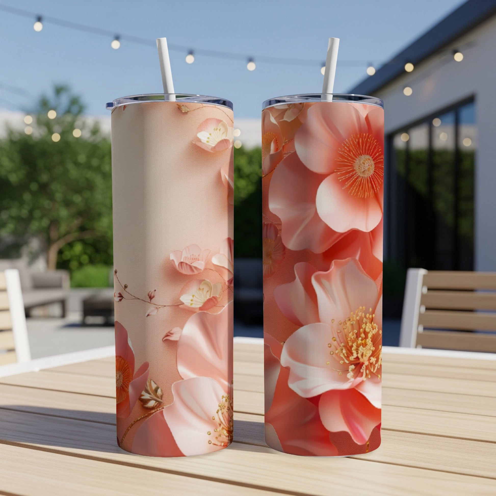 Two tumblers with floral designs and straws on a table outdoors.