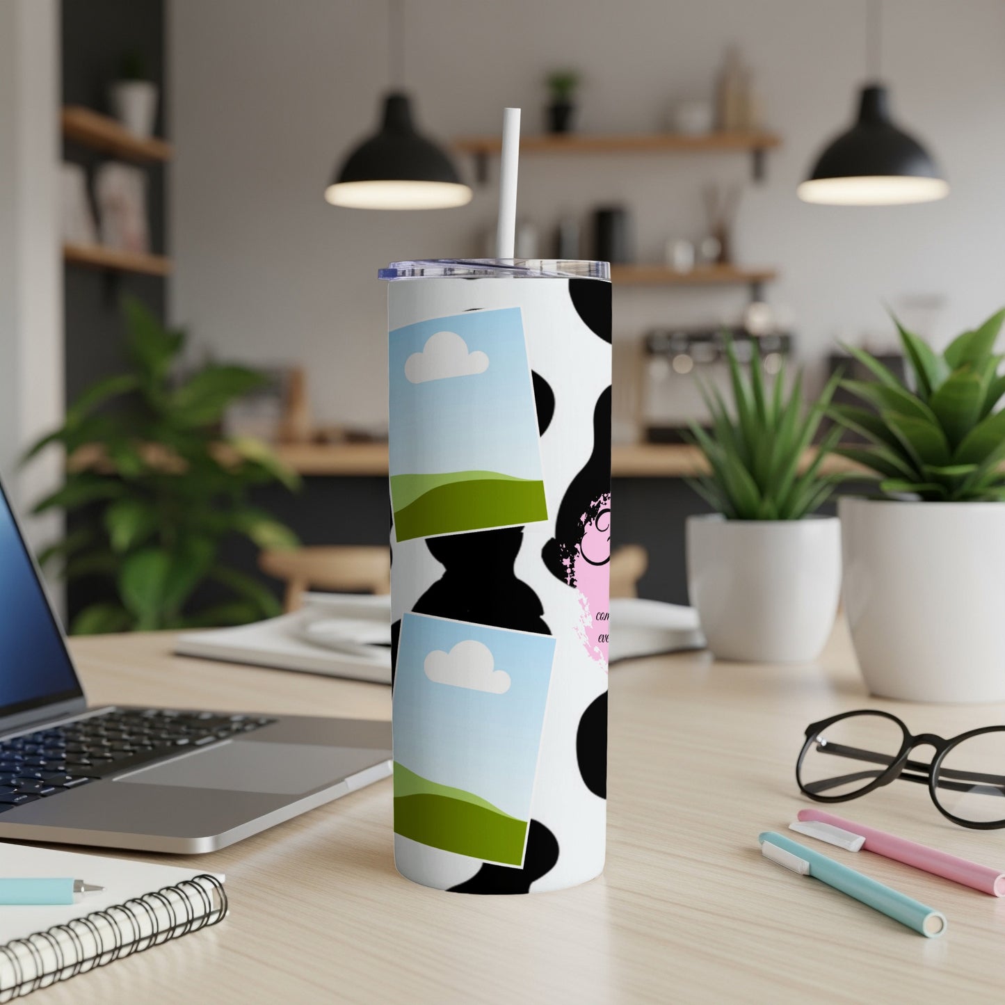 Cow print tumbler with sky and grass graphics and a cartoon face.