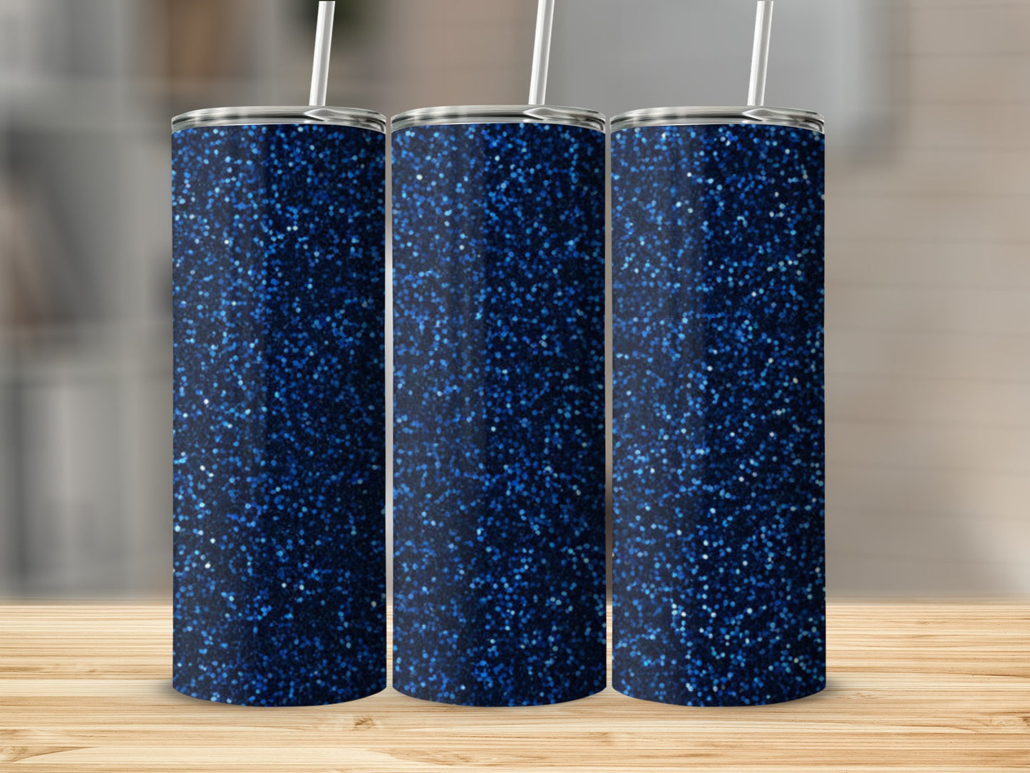 Three navy blue glitter tumblers with white straws on a wooden surface.