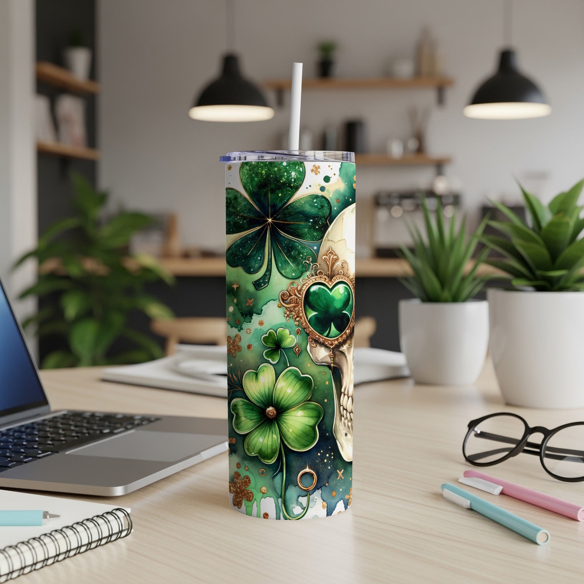 Green shamrock and gold skull patterned tumbler on desk with laptop and pens.