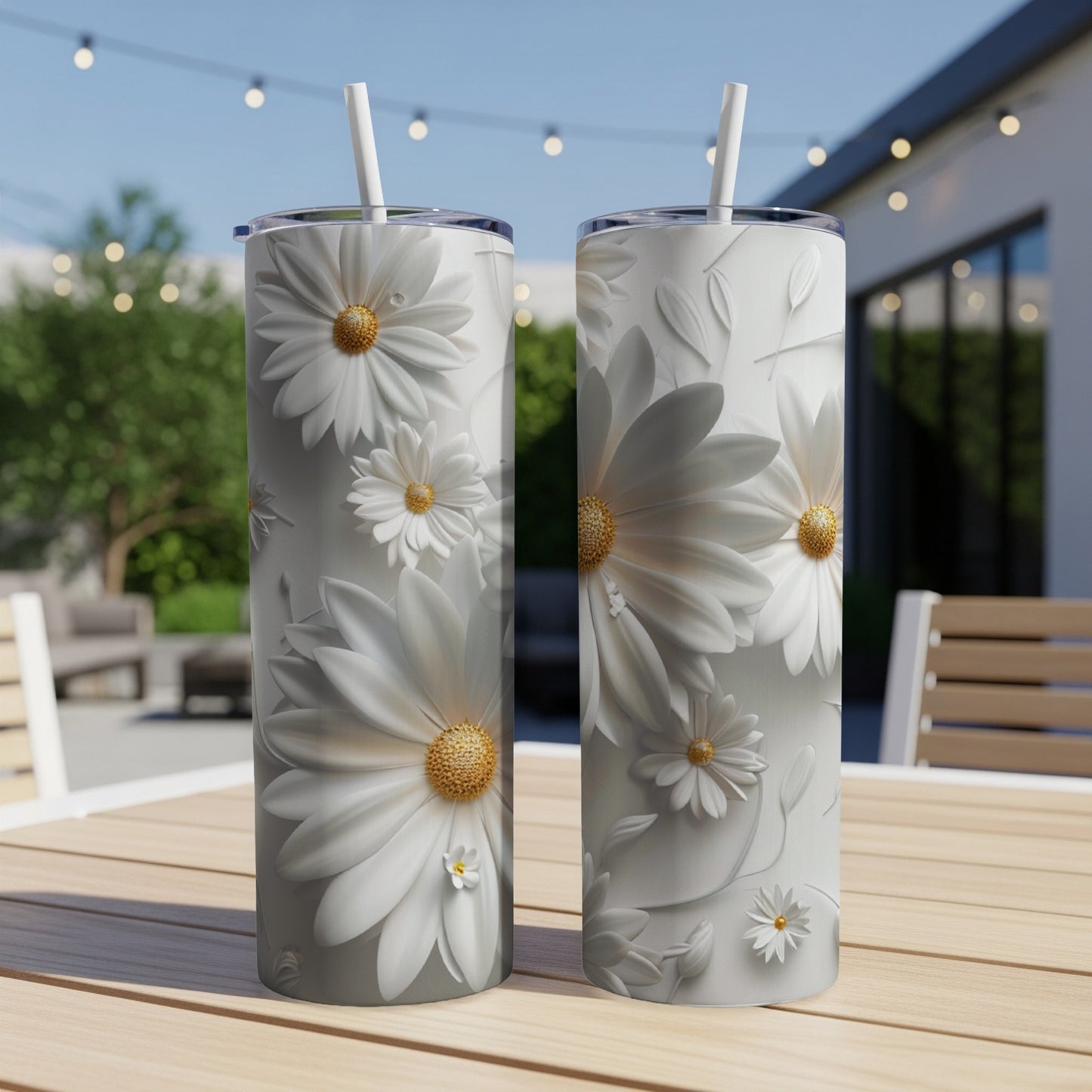 Two white floral tumblers with straws on a wooden table outdoors.