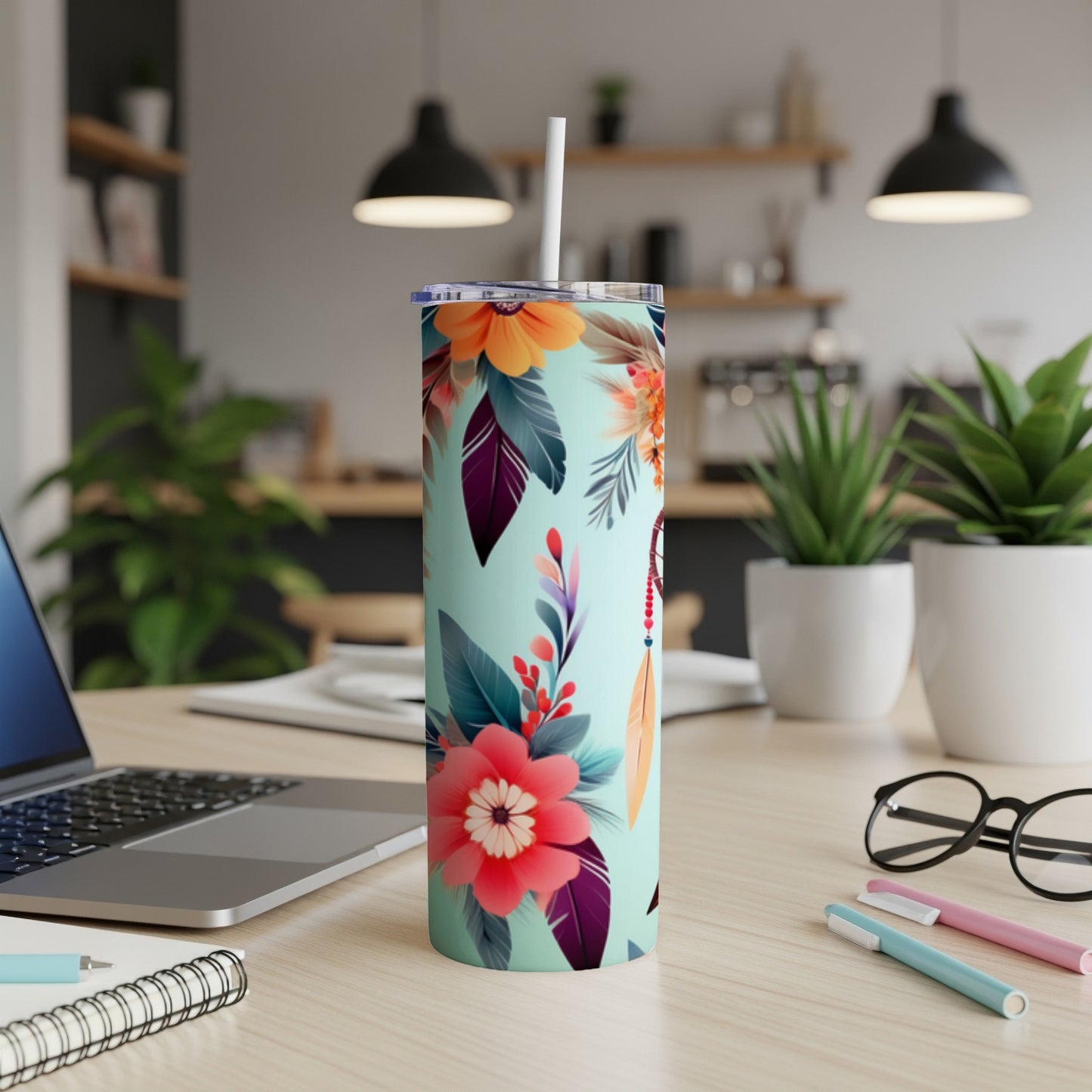 Mint green tumbler with floral and feather design, on a desk.