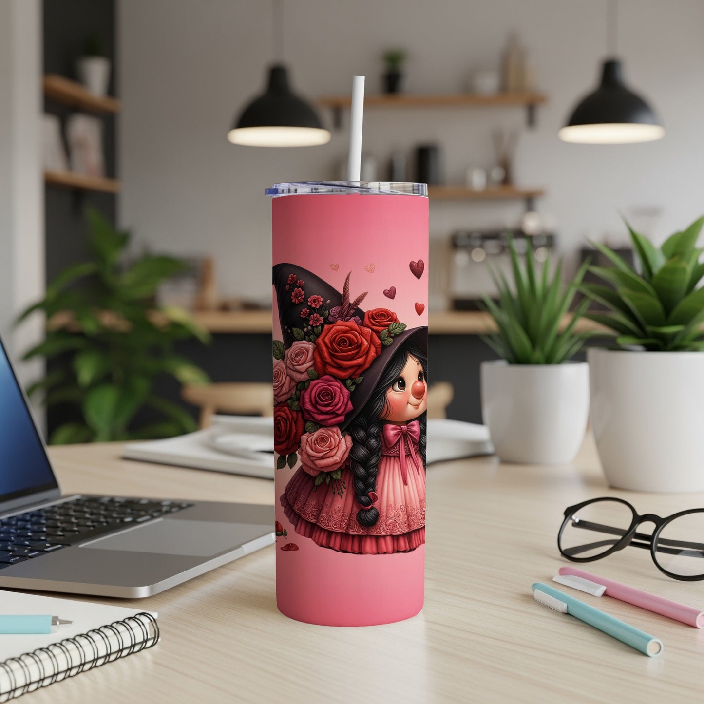 Pink tumbler with cartoon witch holding flowers, on desk.