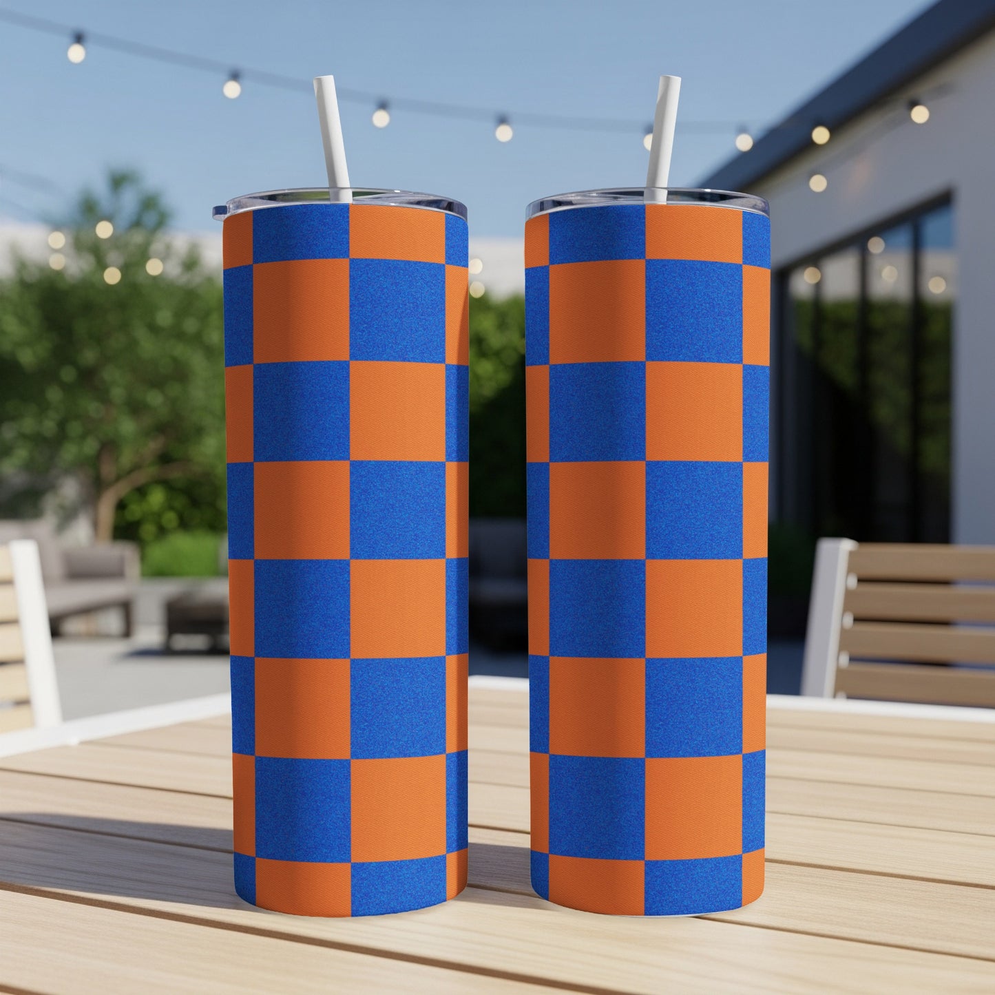 Two checkered blue and orange tumblers with straws on a wooden table.